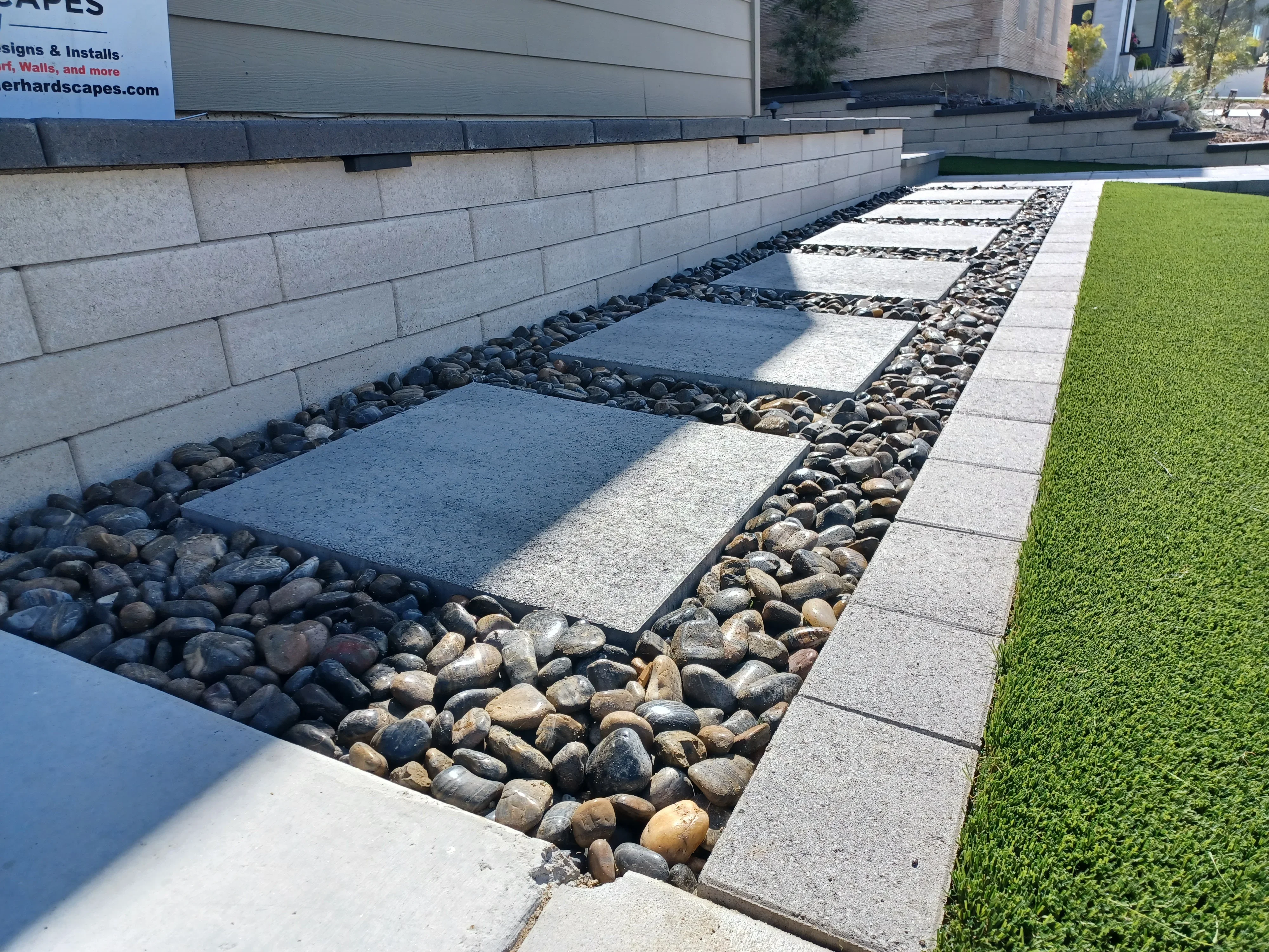 Concrete retaining wall with river rock, permeable pavers, and synthetic turf landscaping