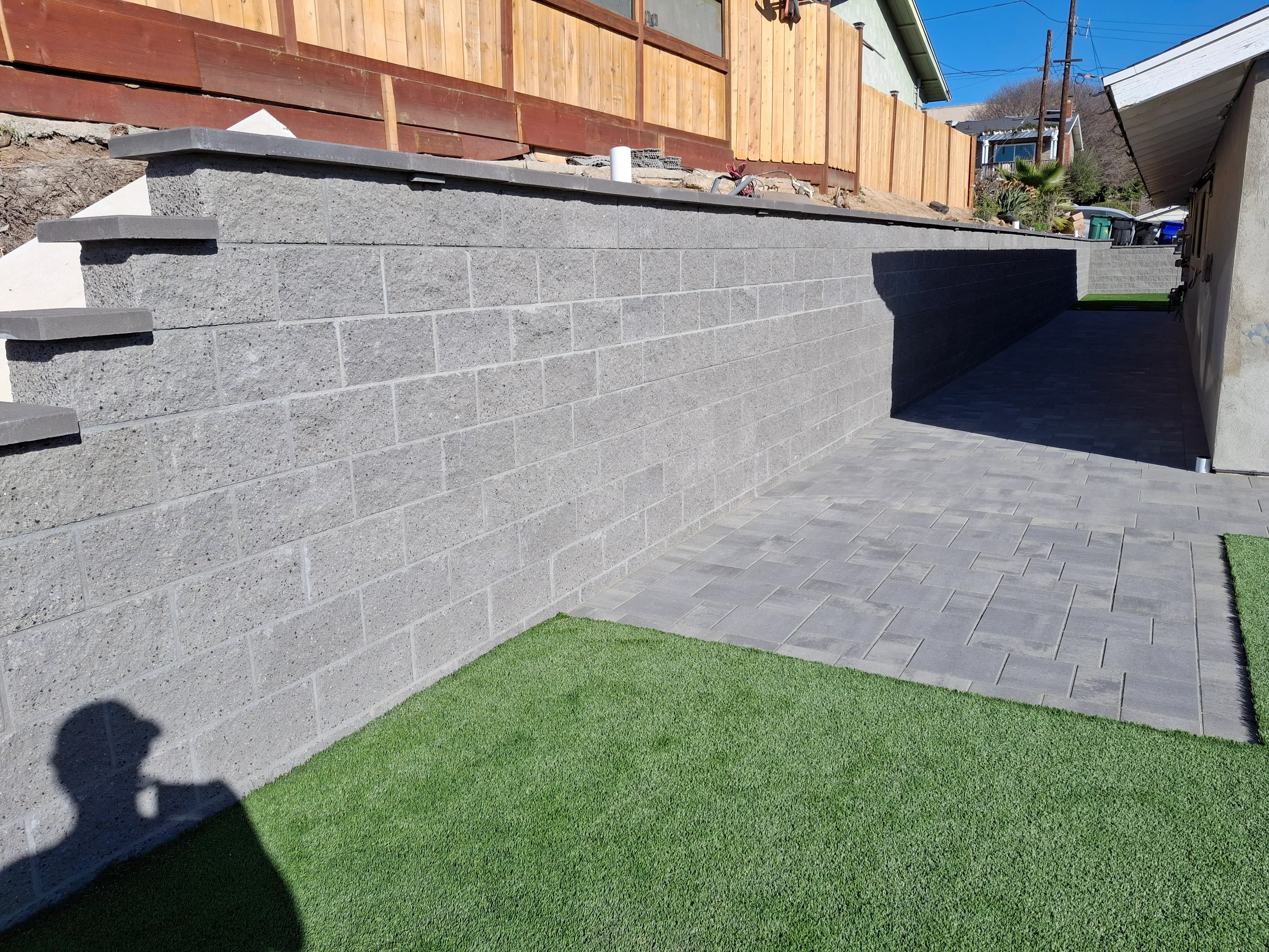 Gray concrete block retaining wall with black caps and gray paver patio installation