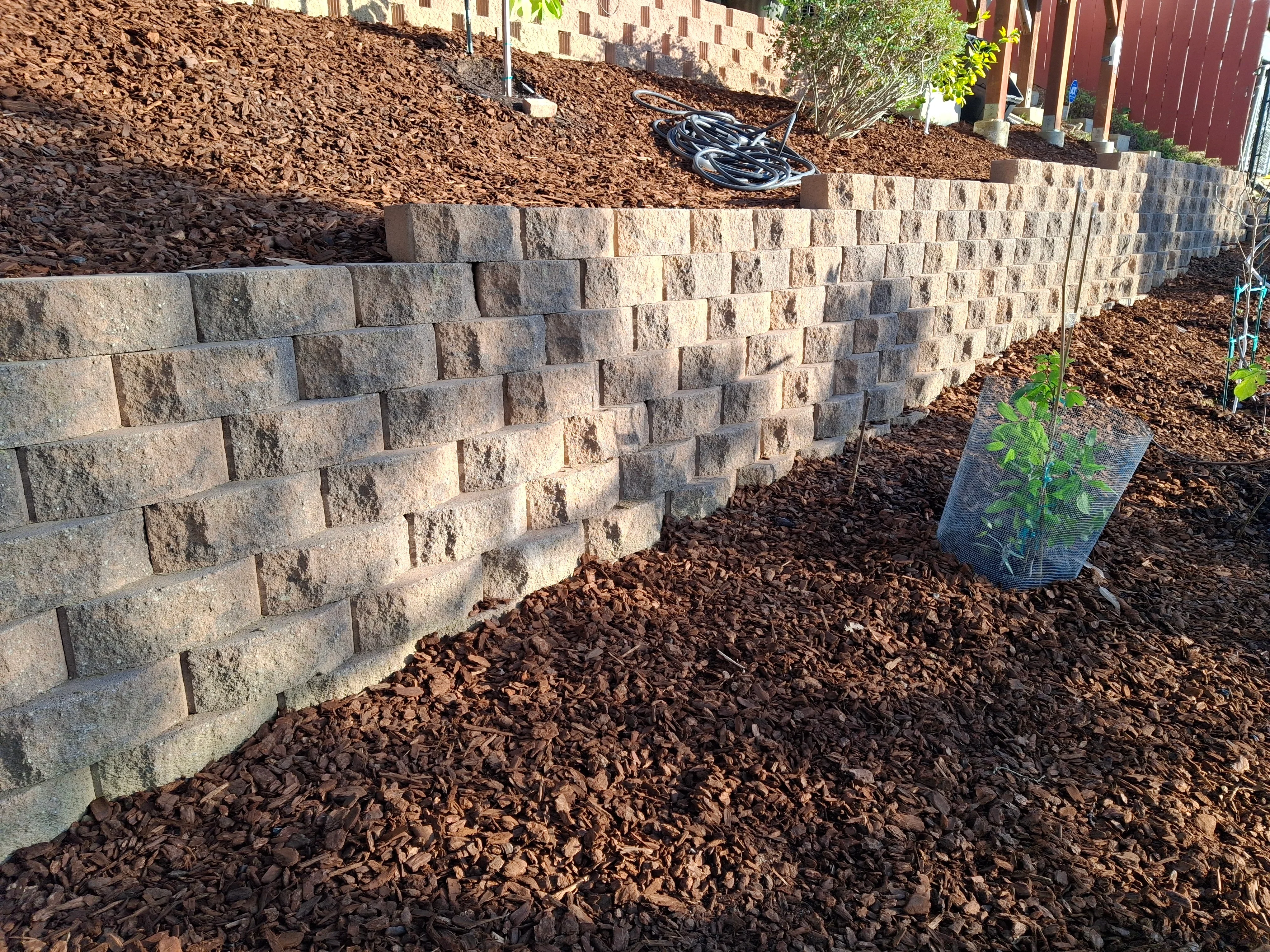 Stacked concrete paver retaining wall with brown mulch and planted landscaping