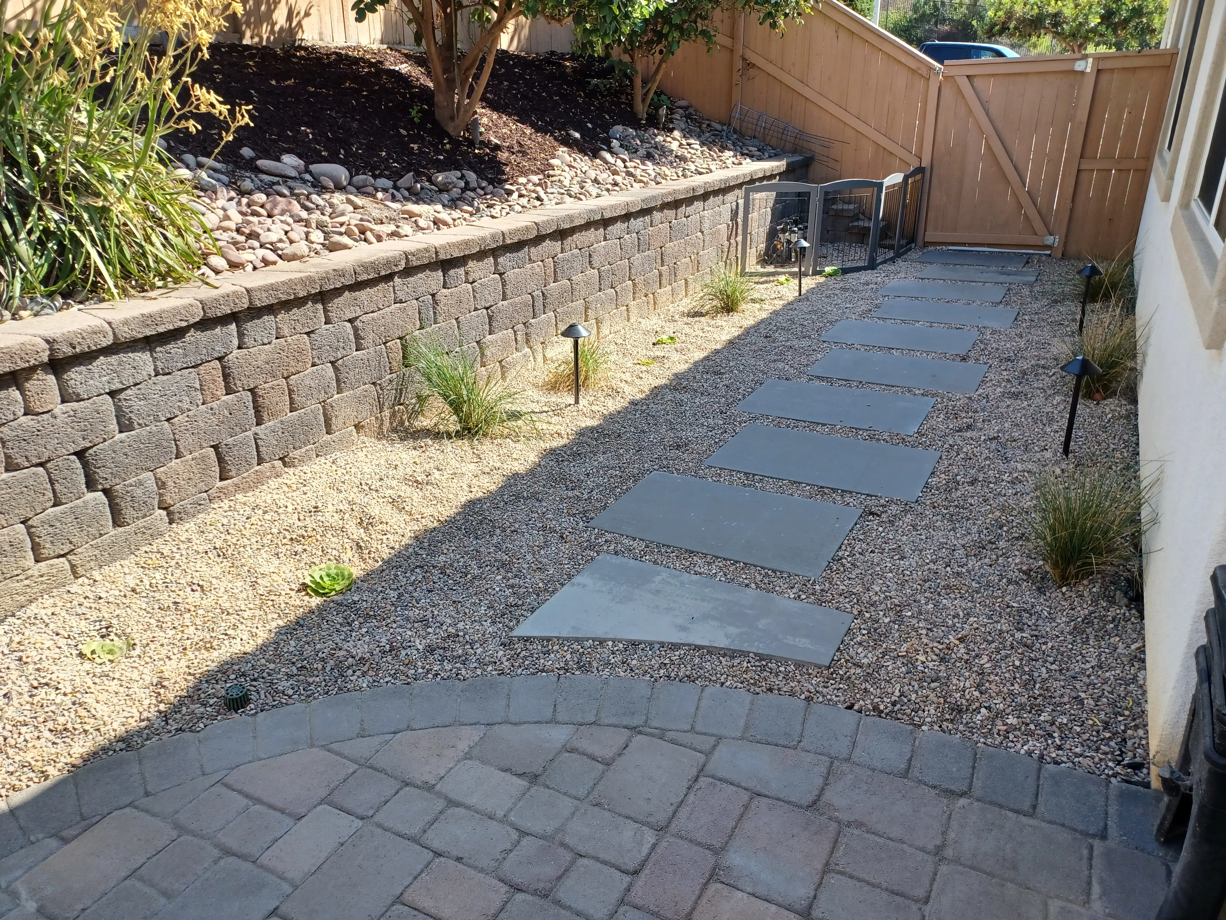 Segmental retaining wall, gray stepping stones, crushed gravel base, and landscape lighting in backyard