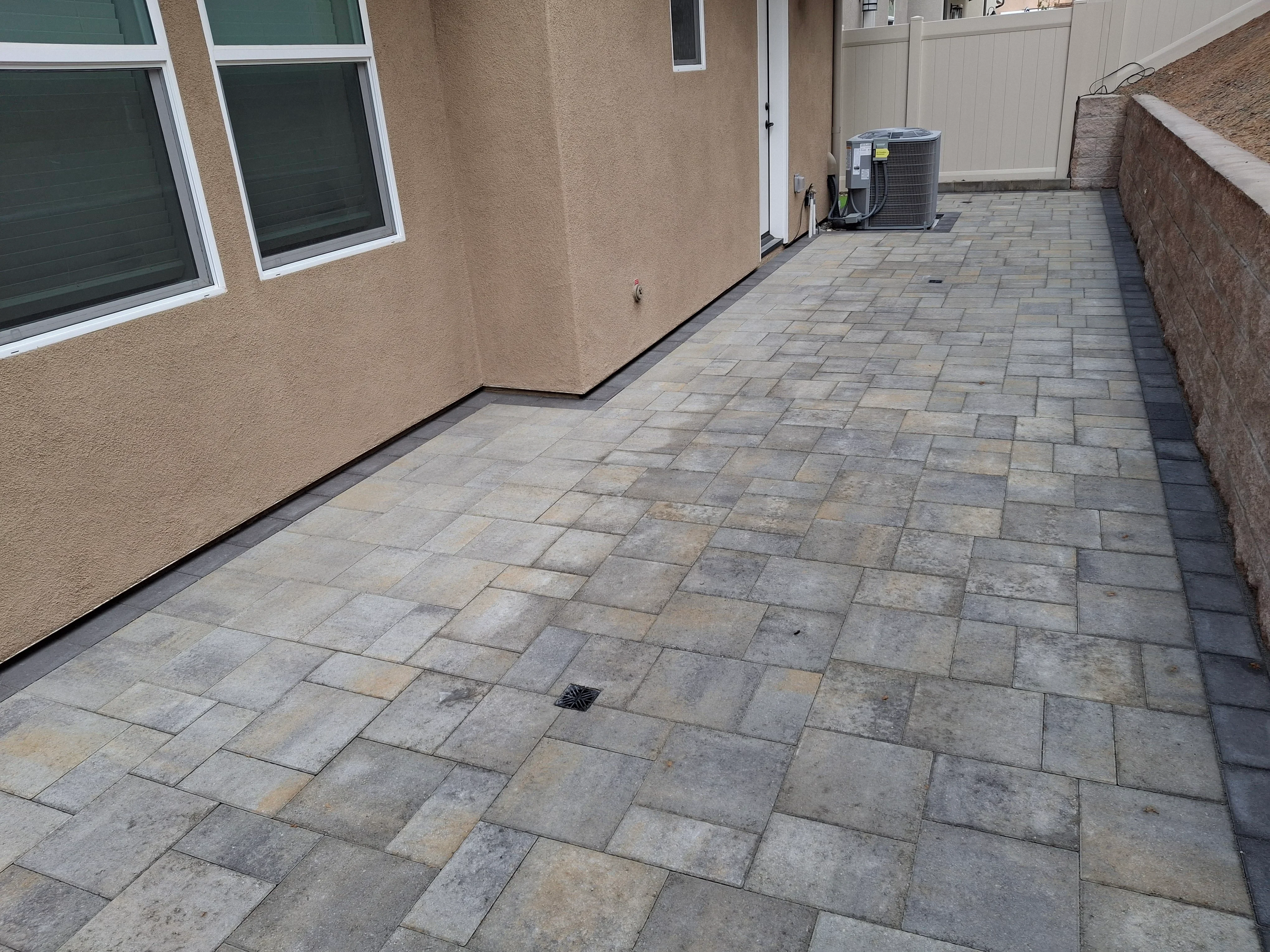 Gray and tan concrete pavers in running bond pattern with drainage grate