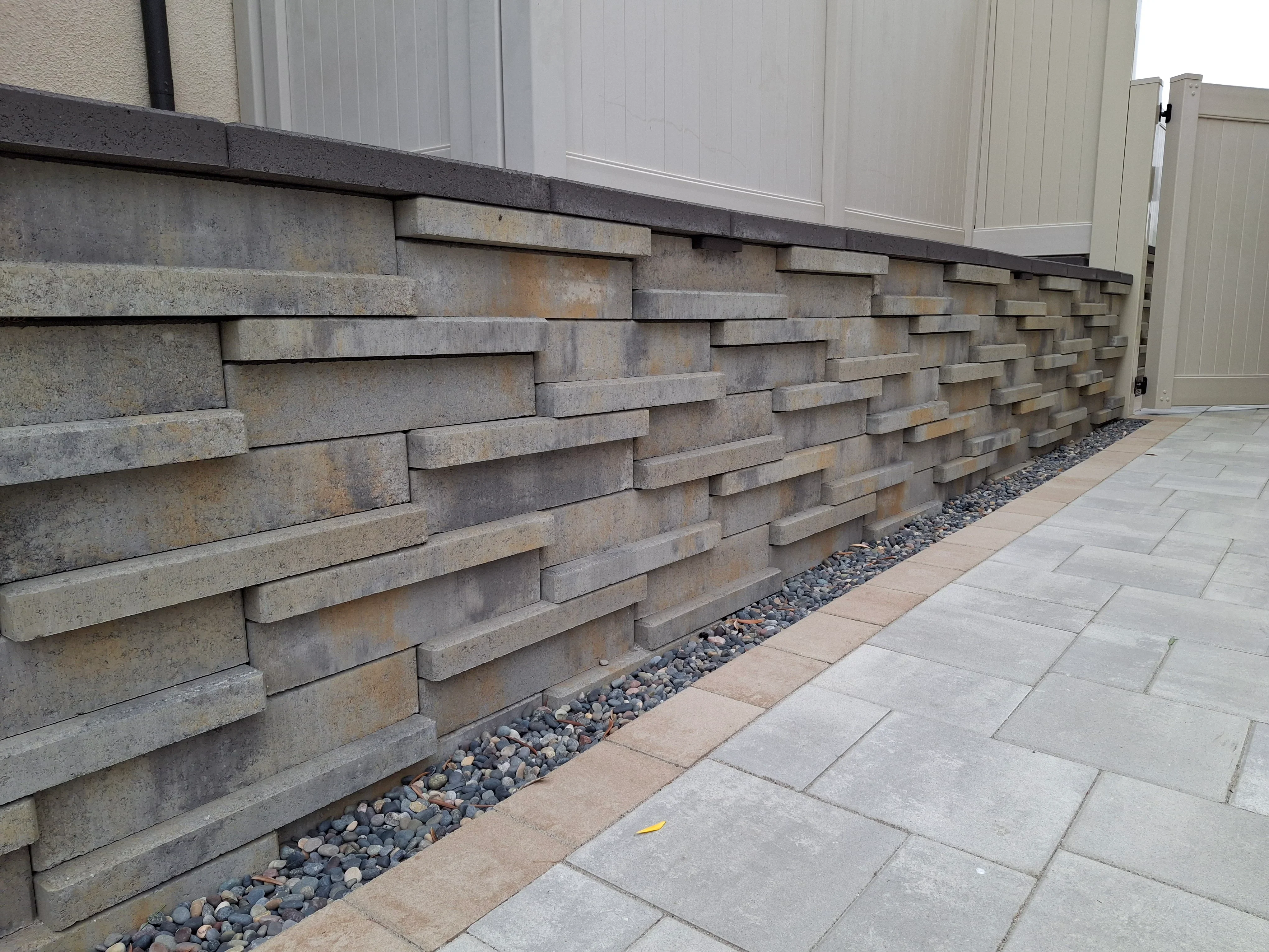 Stacked stone retaining wall with staggered concrete blocks, gravel drainage, and concrete paver walkway