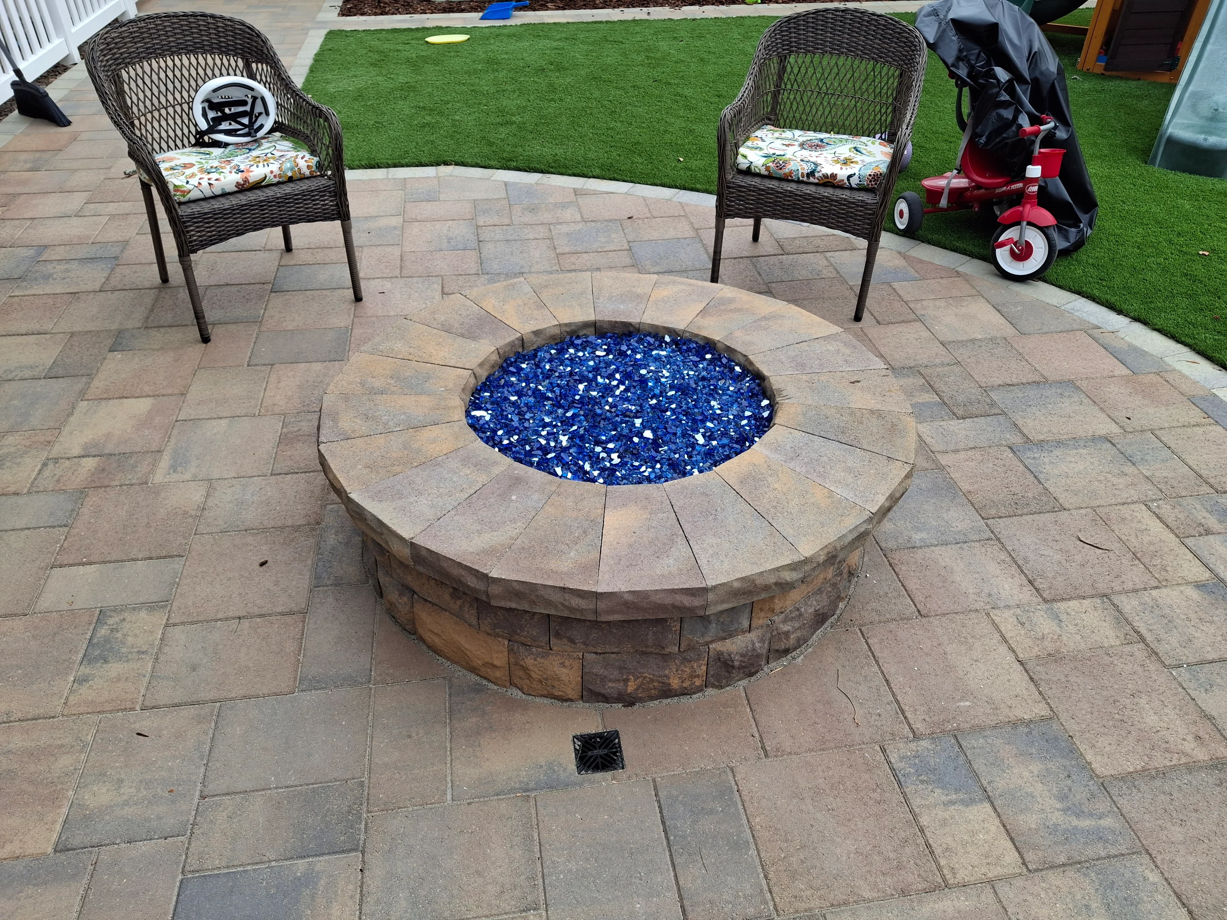 Circular stone fire pit with blue glass media on paver patio with seating