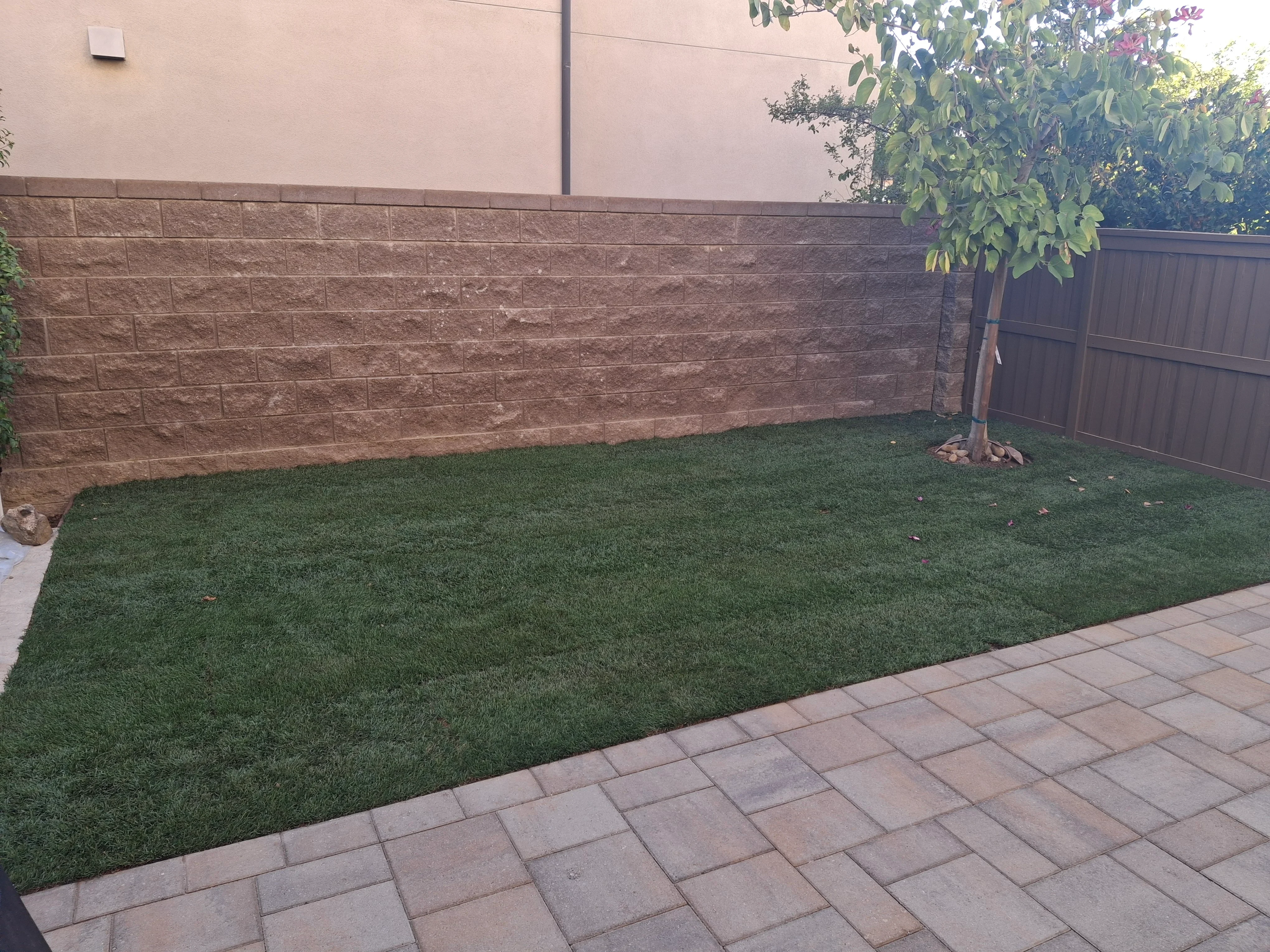 Concrete block retaining wall with decorative paver patio and installed turf lawn