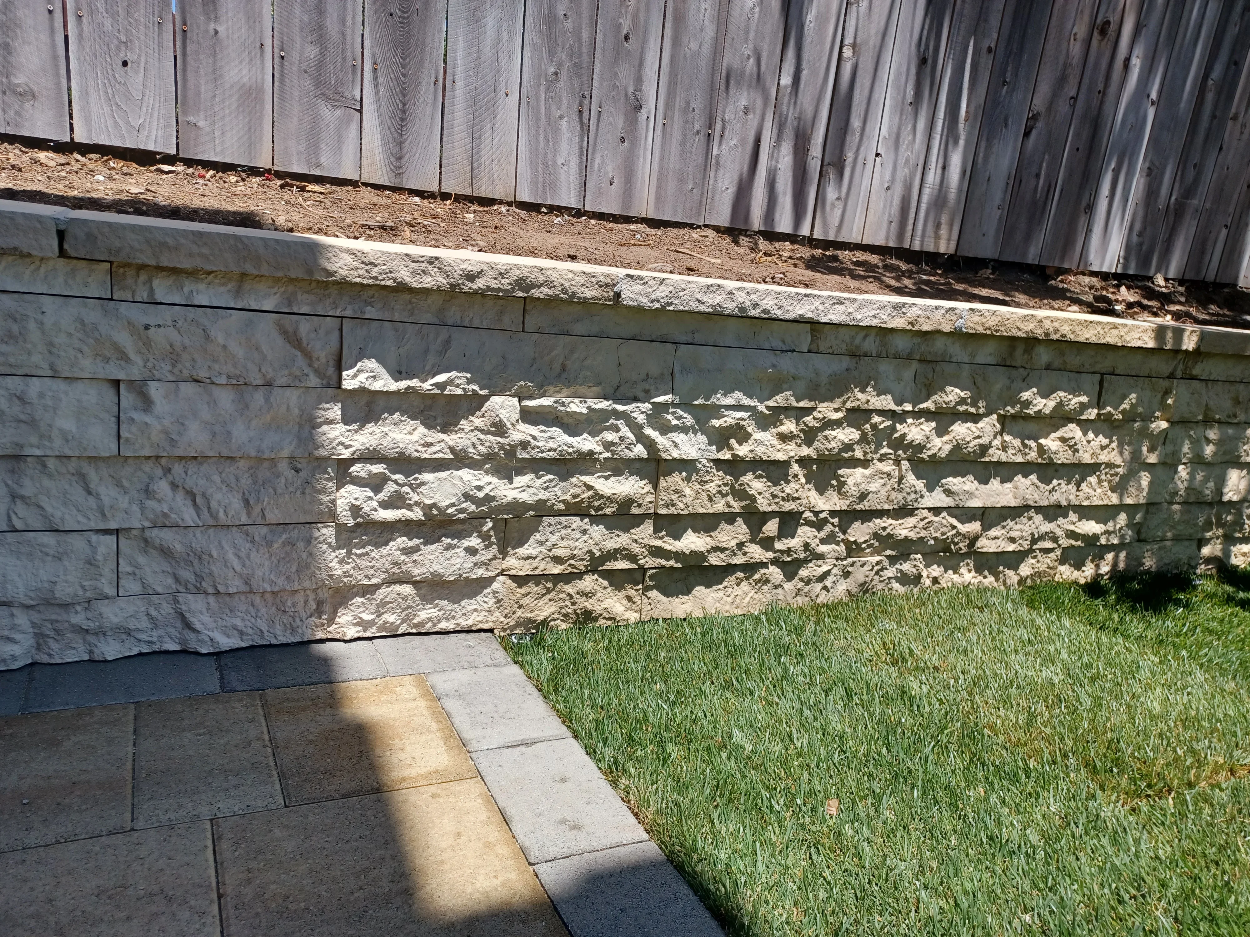 Stacked stone retaining wall with split-face blocks and concrete paver patio base