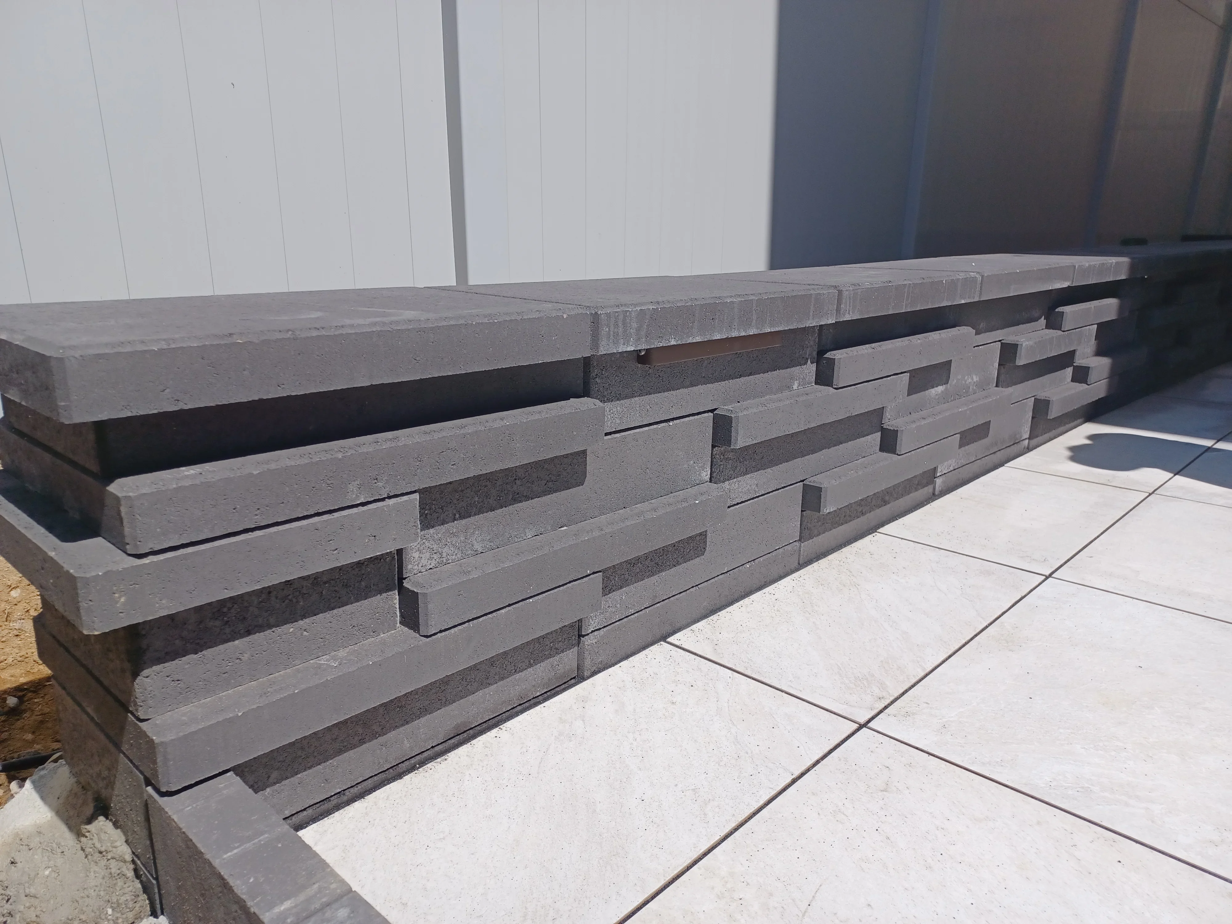 Stacked gray concrete retaining wall with integrated seating ledge and paver patio
