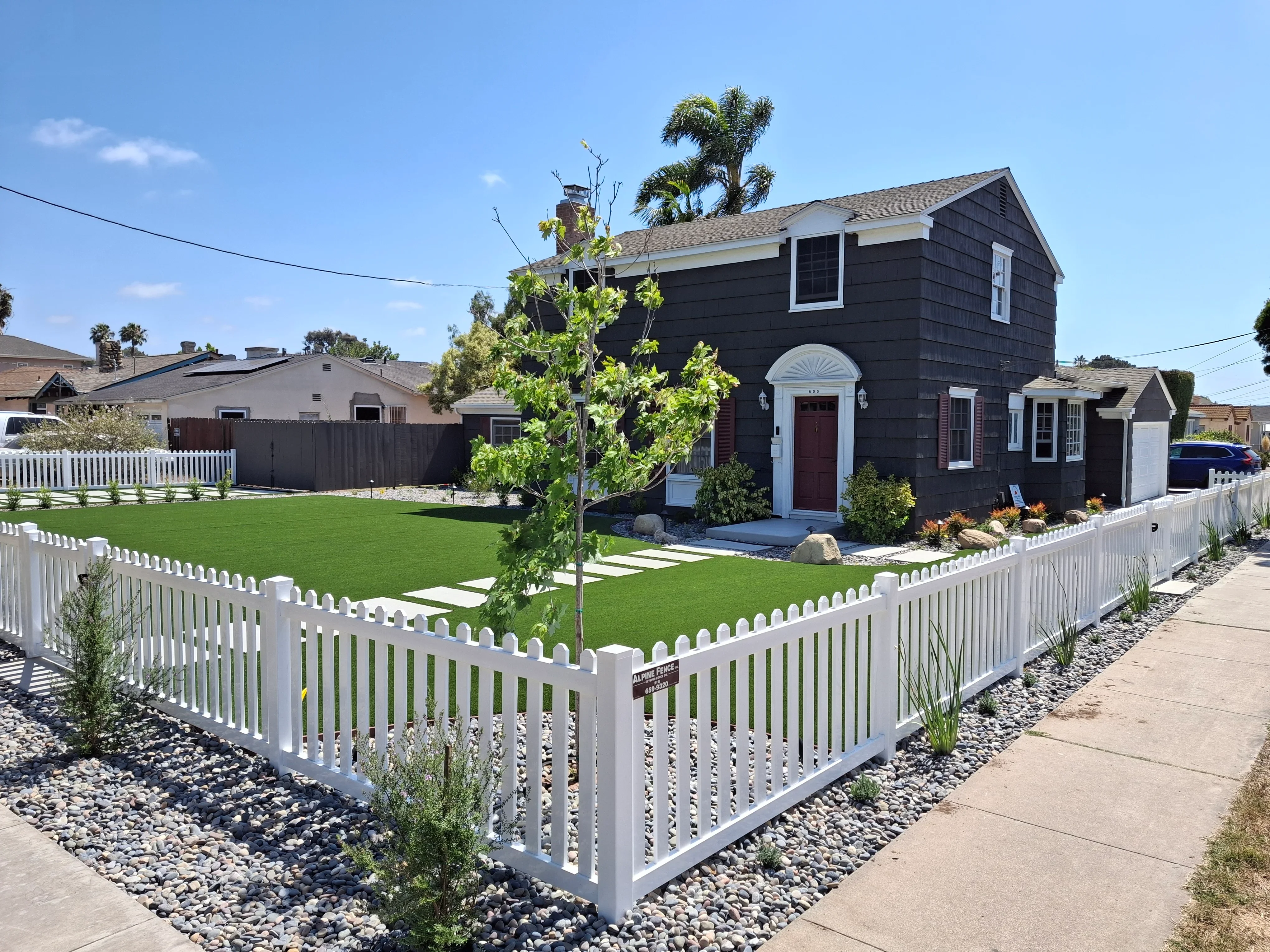 White picket fence, paver walkway, and river rock hardscape around cottage home