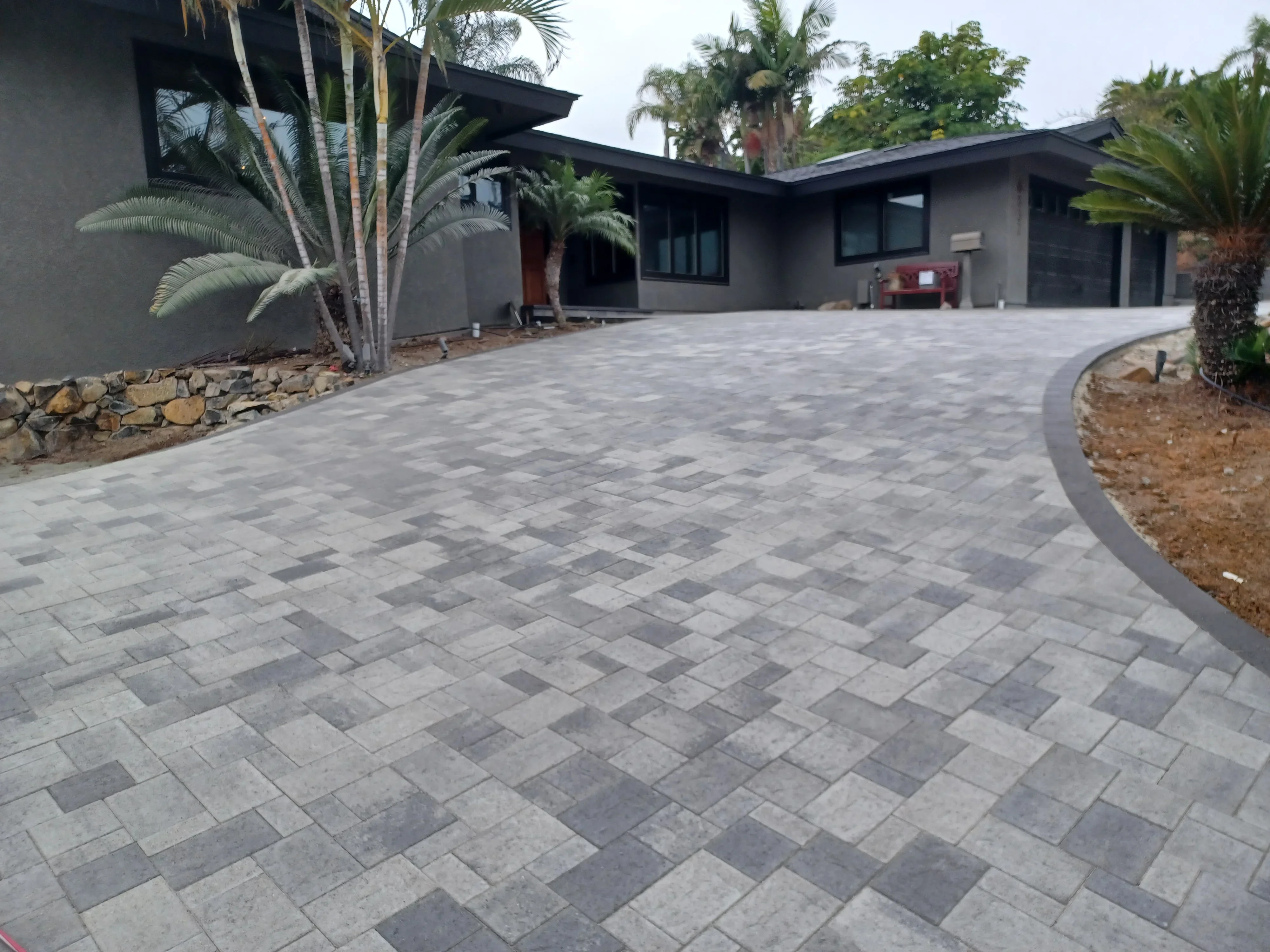 Gray permeable pavers in herringbone pattern with curved metal edging and landscape beds
