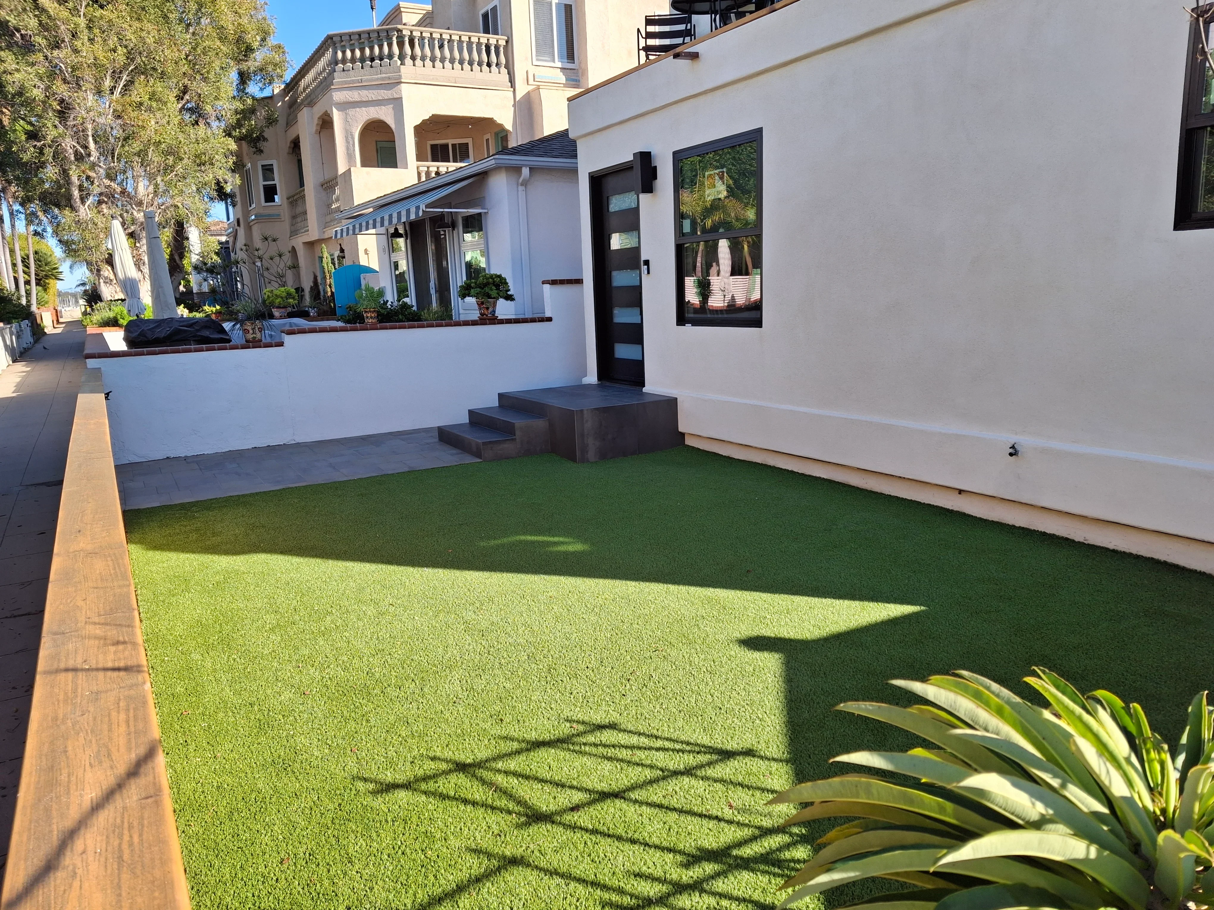 Synthetic turf courtyard with black composite deck platform, white stucco walls, and integrated planters