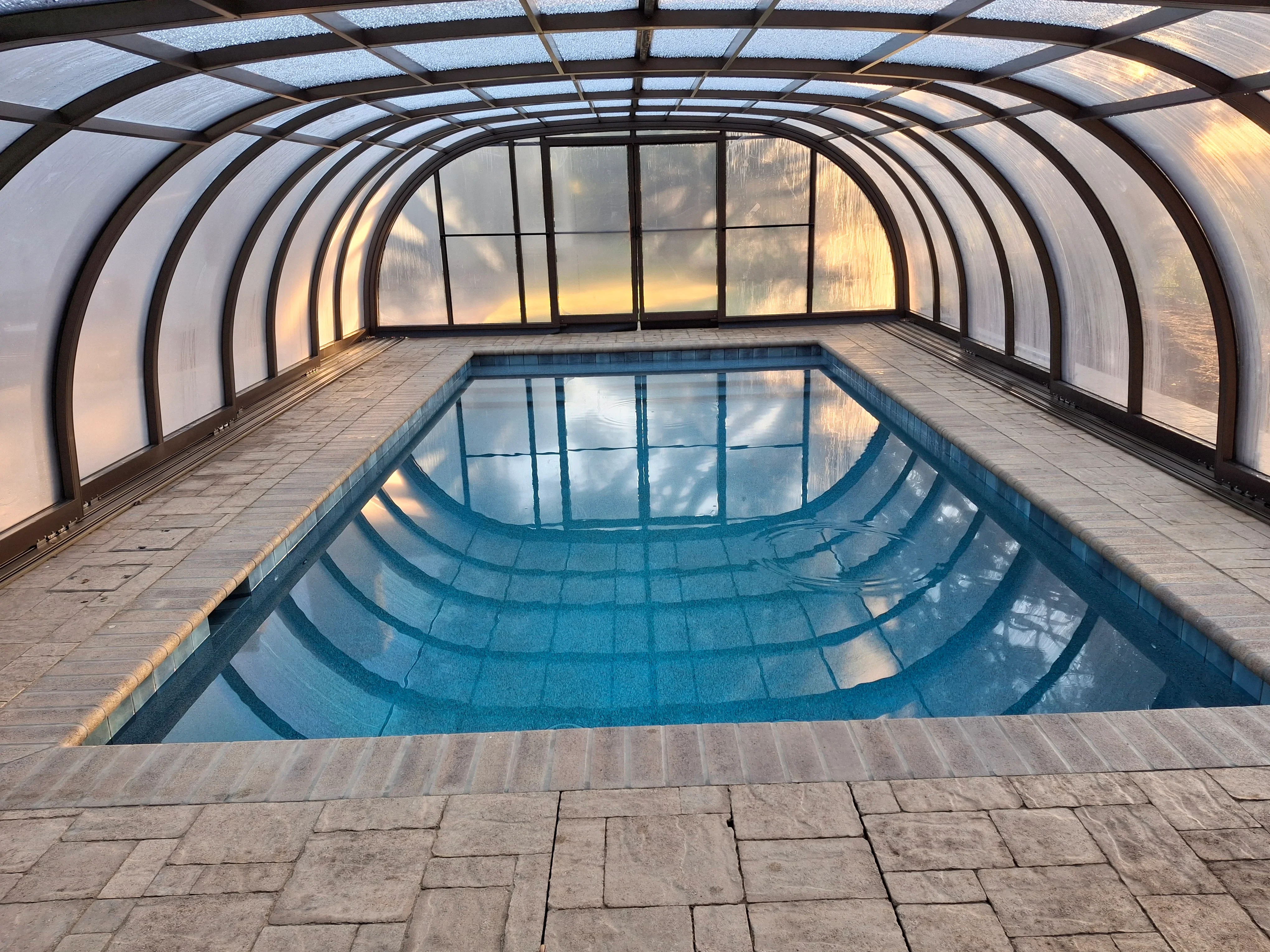 Arched polycarbonate pool enclosure with aluminum frame and gray paver deck