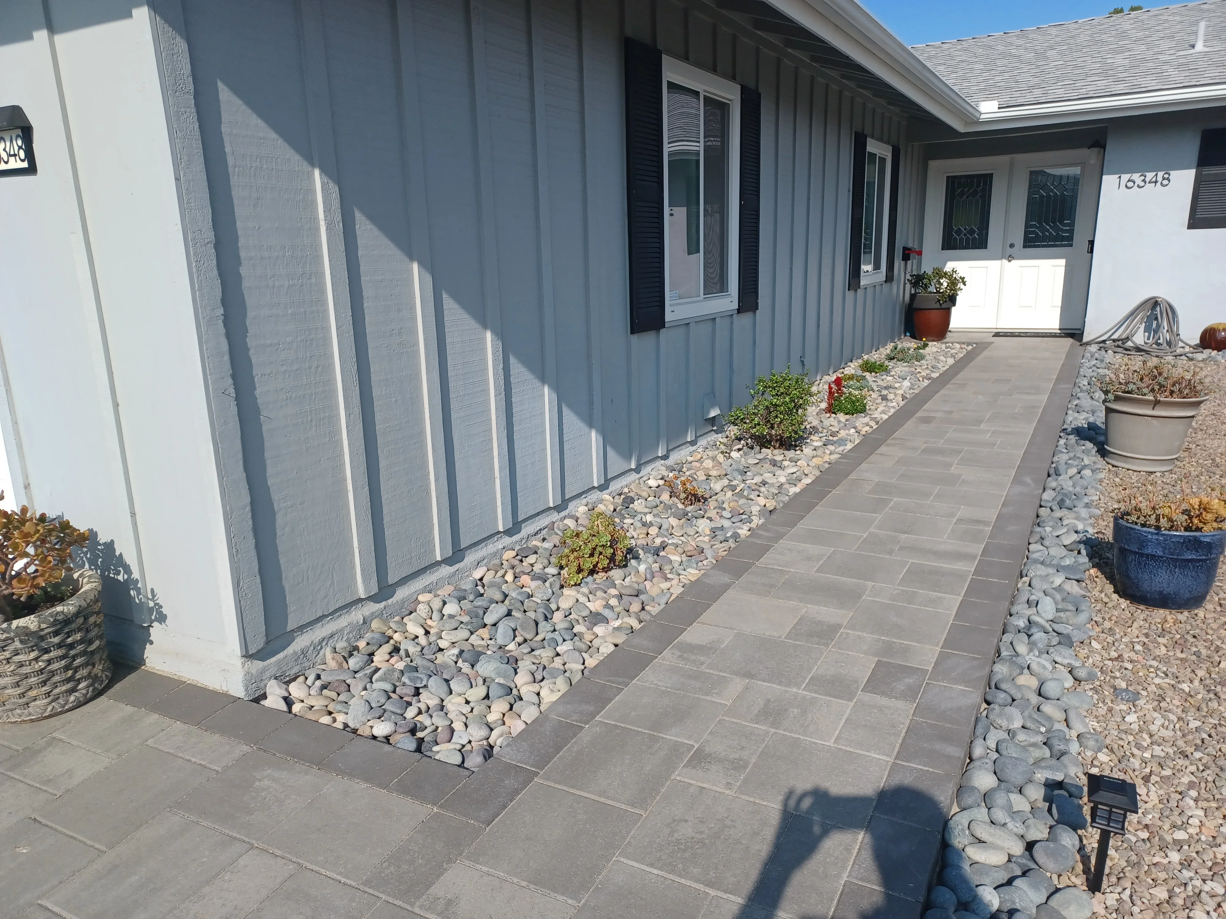 Gray paver walkway with river rock borders and planted beds along mobile home entry