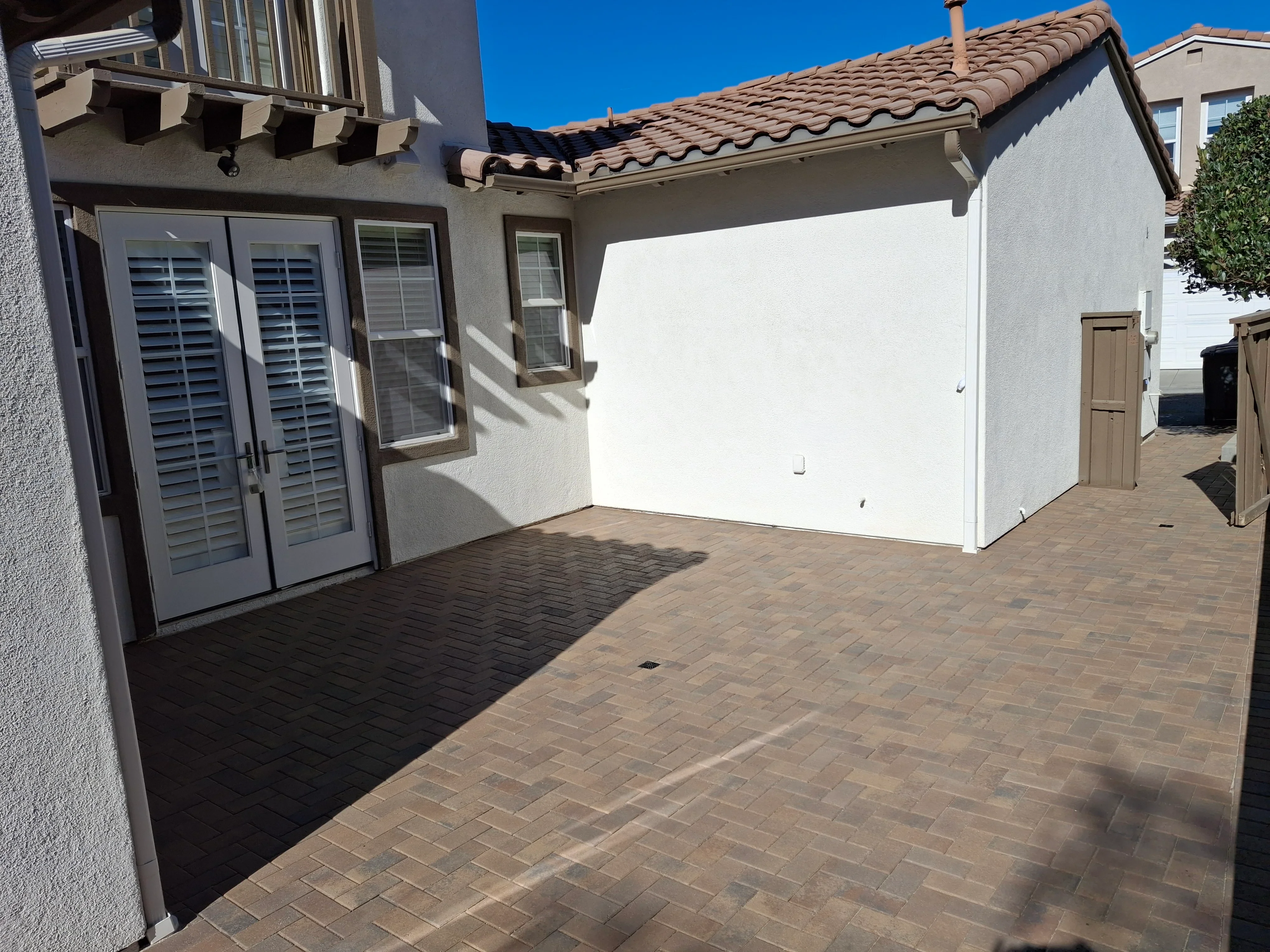 Herringbone paver patio with white stucco wall and clay tile roof detail
