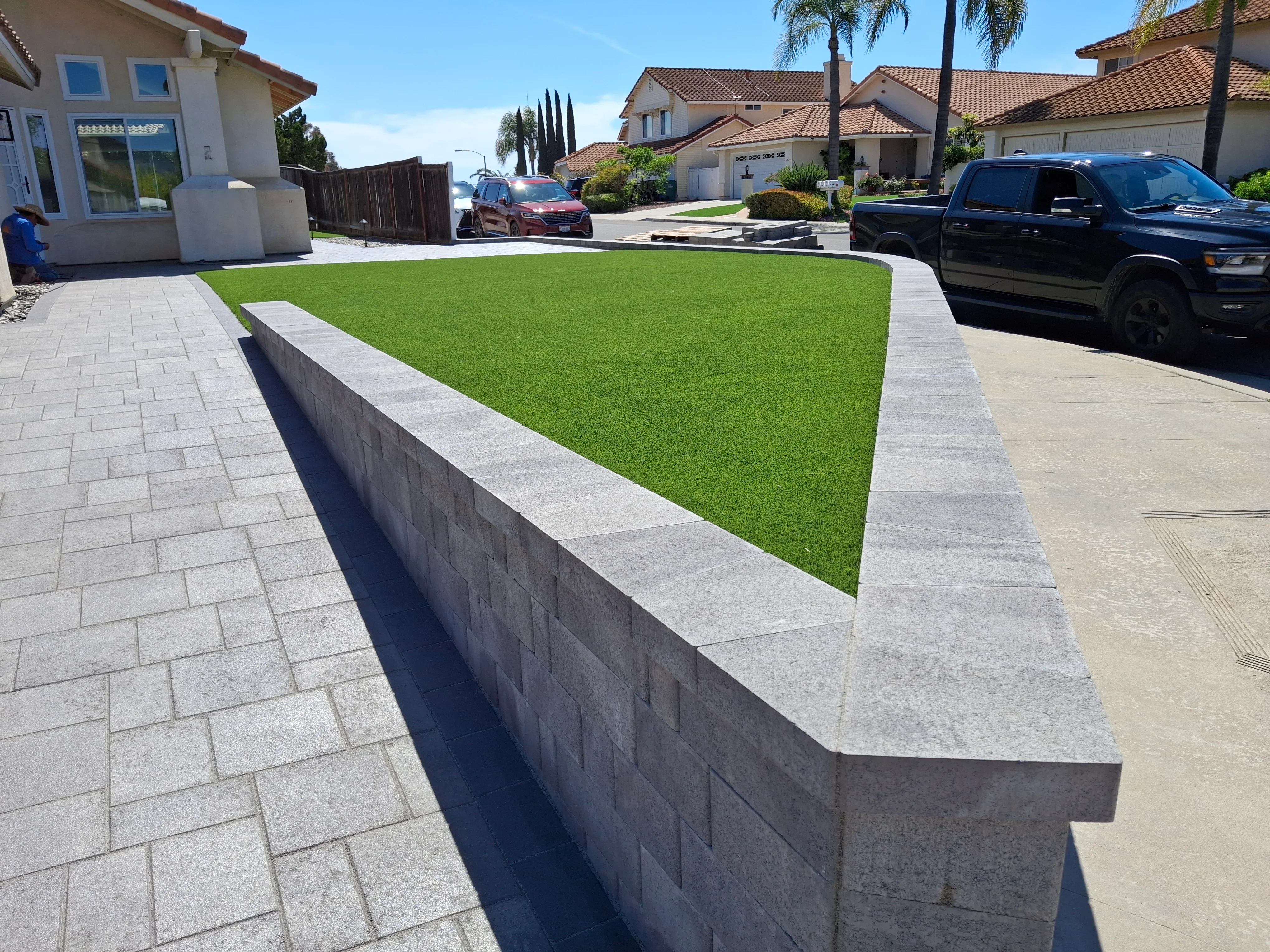 Gray concrete block retaining wall with synthetic turf lawn and paver edging in residential front yard