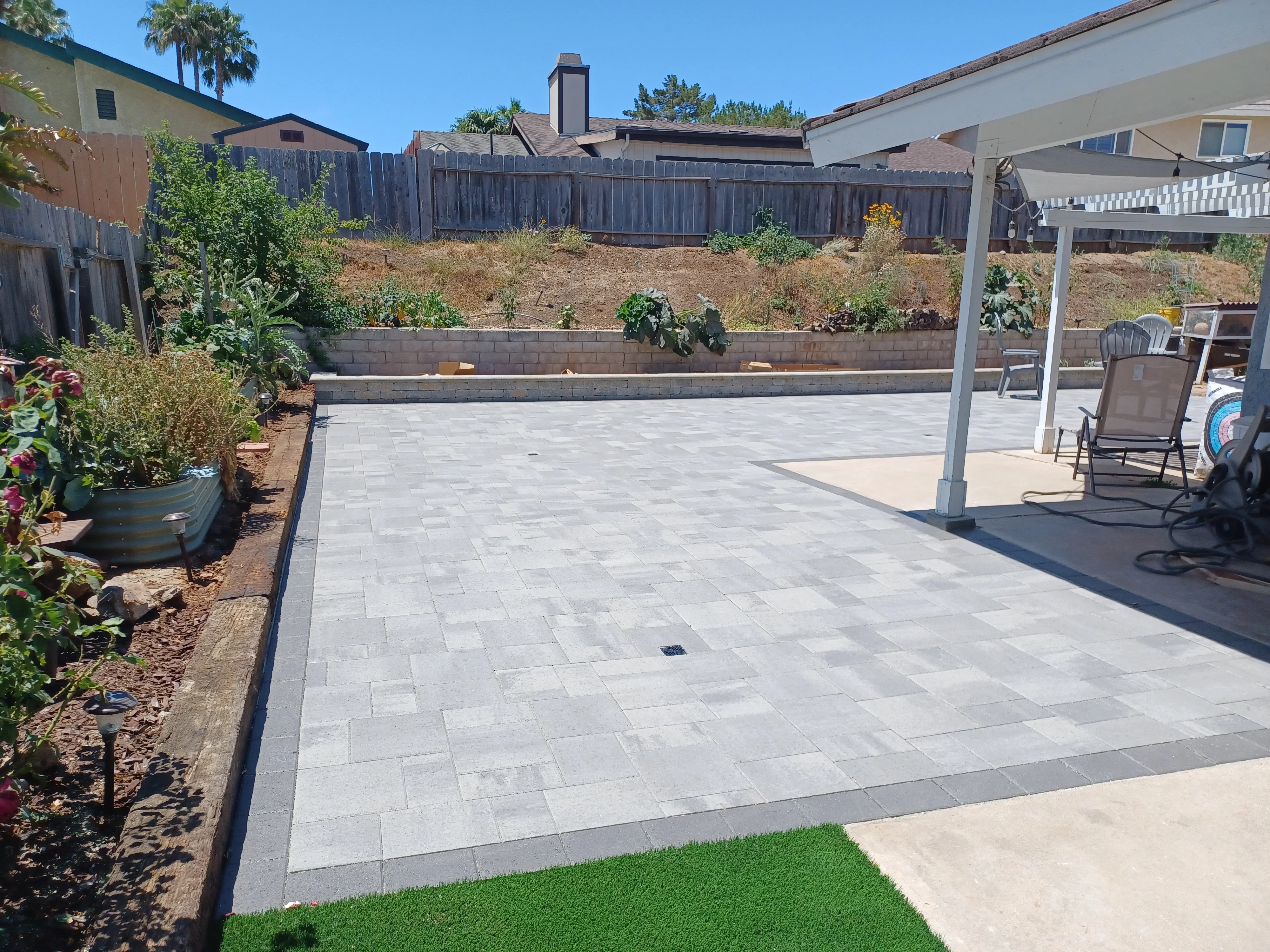 Gray permeable paver patio with raised concrete planter wall and aluminum pergola