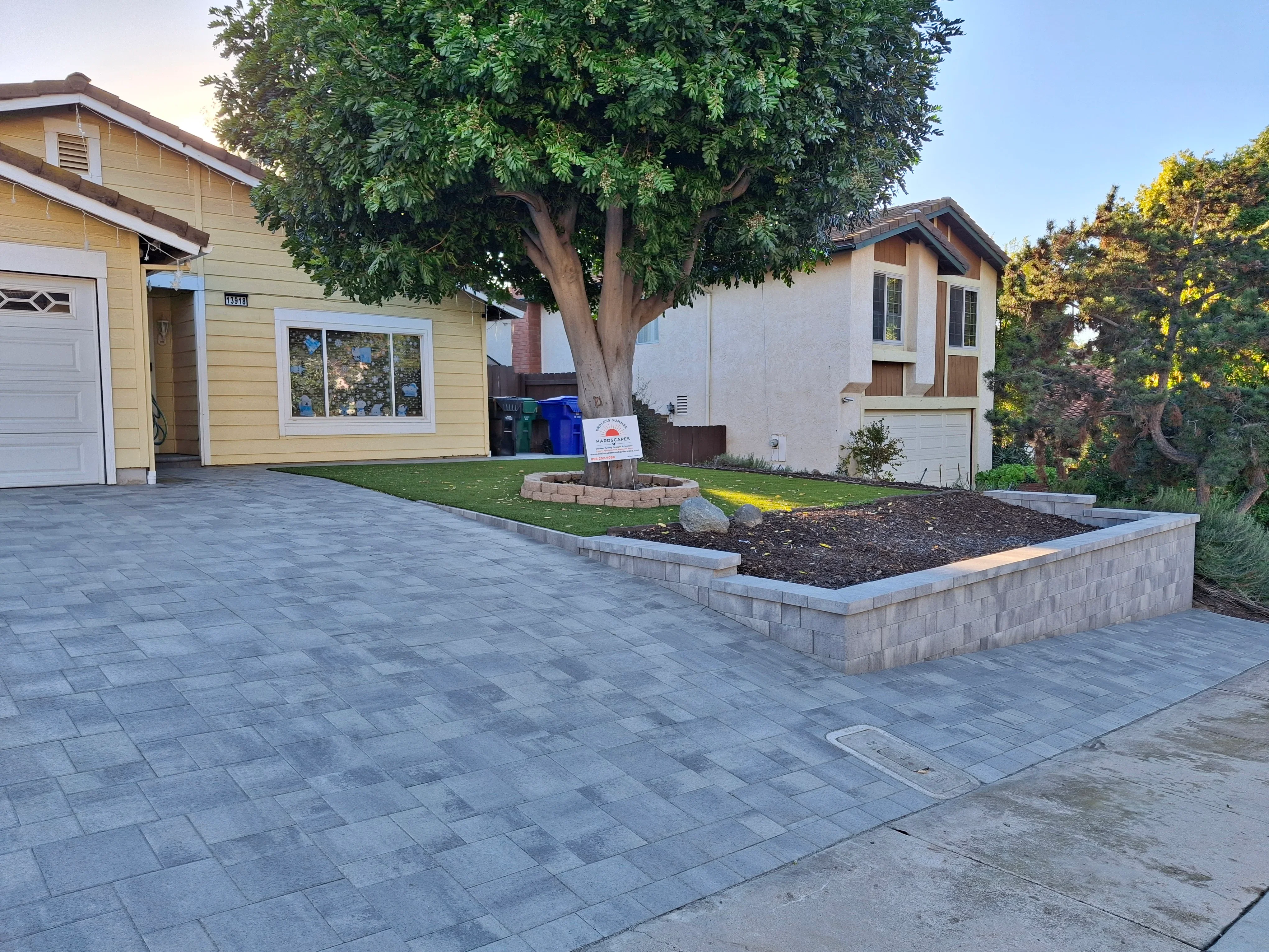 Gray permeable pavers with concrete block raised planter bed and mulch landscaping