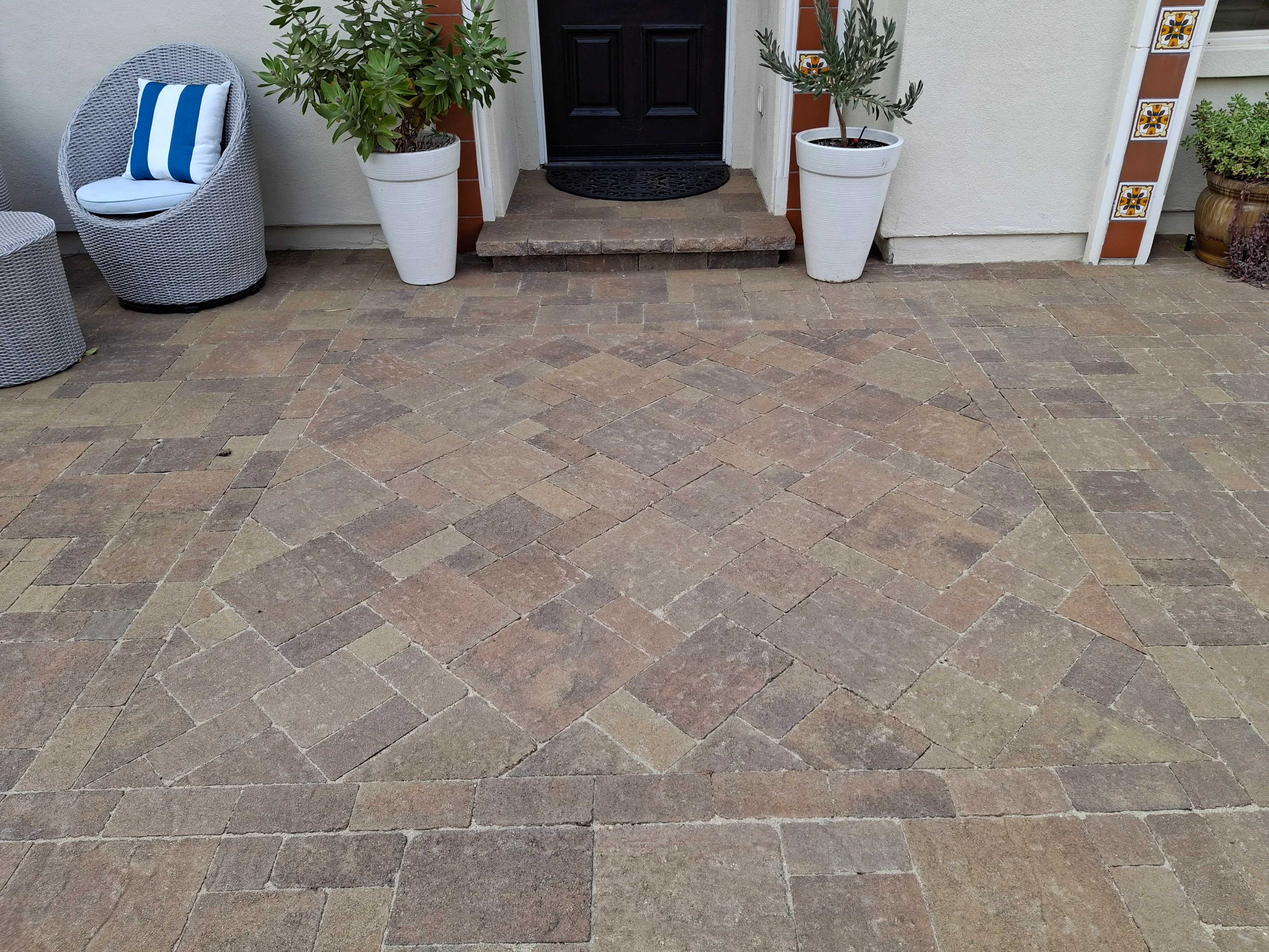 Herringbone paver entryway with rectangular concrete pavers in earth tones and white planter pots