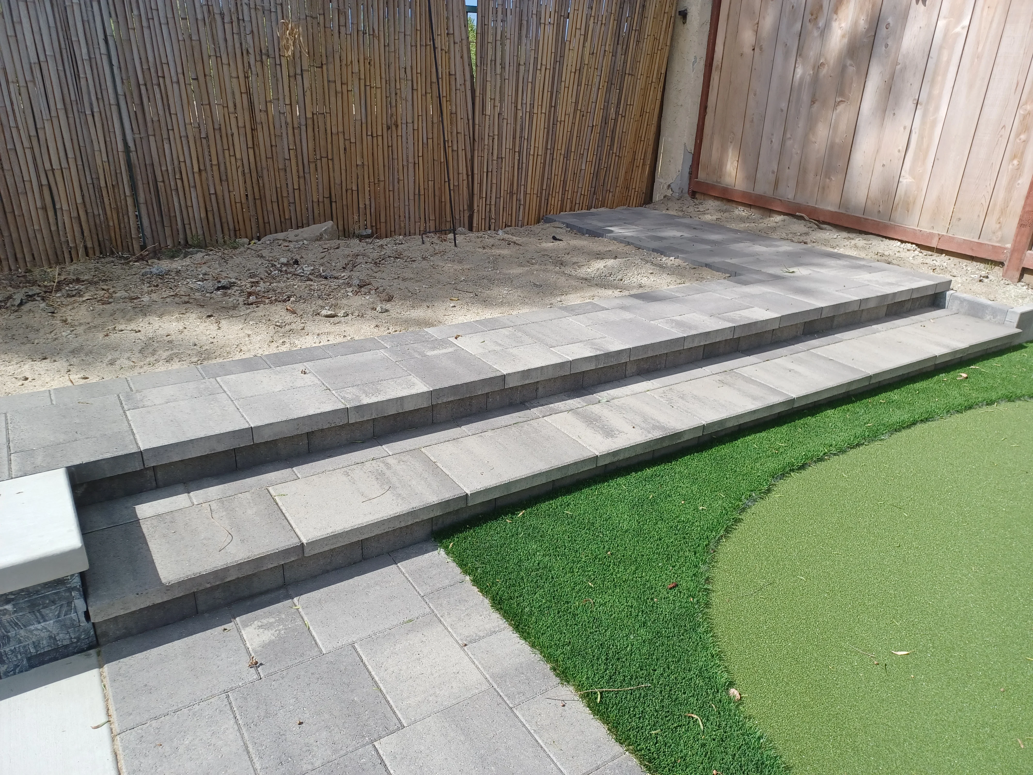 Tiered concrete paver patio with dark retaining walls and artificial turf edging