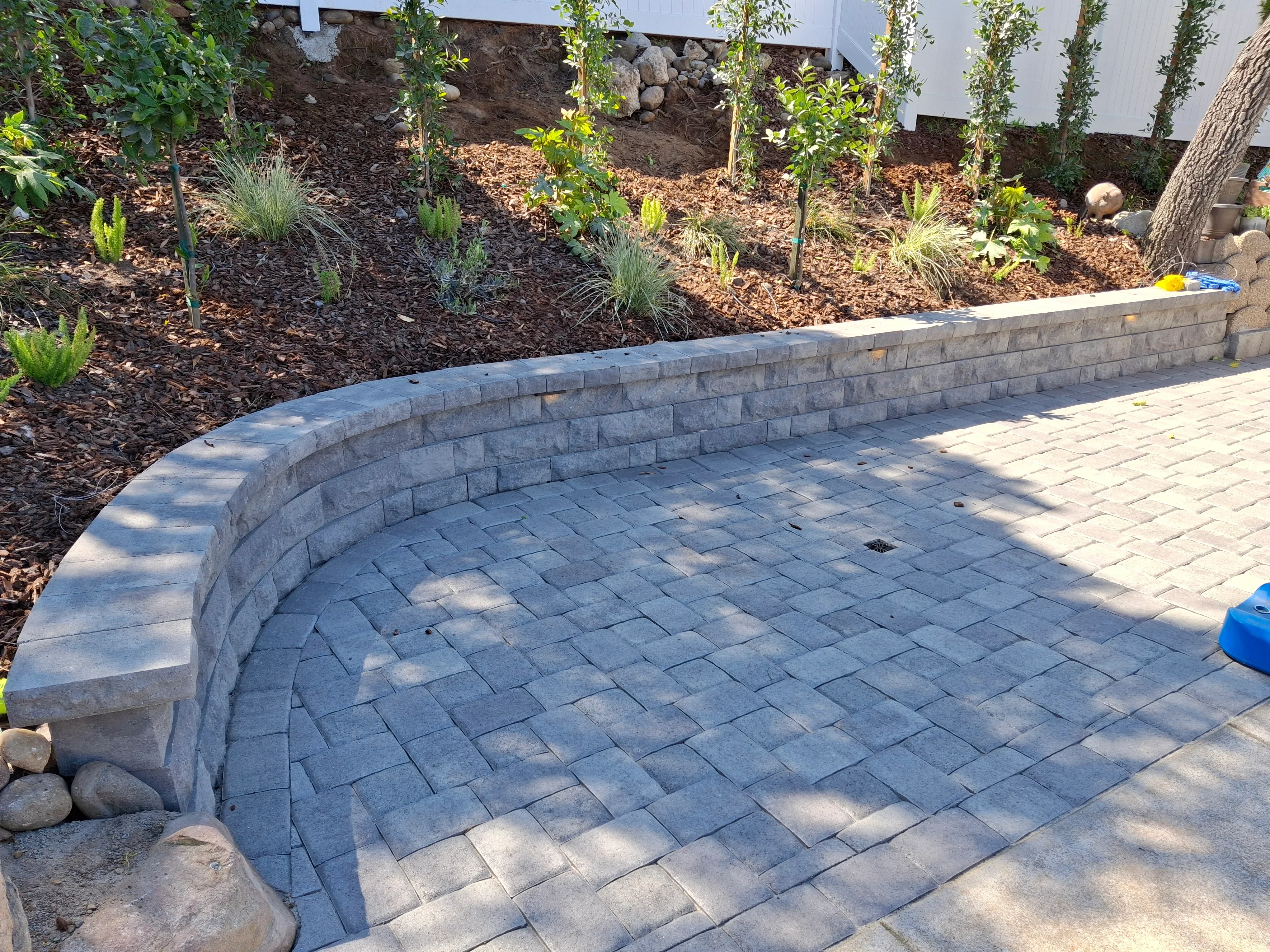 Curved gray concrete paver patio with matching curved retaining wall and planted beds