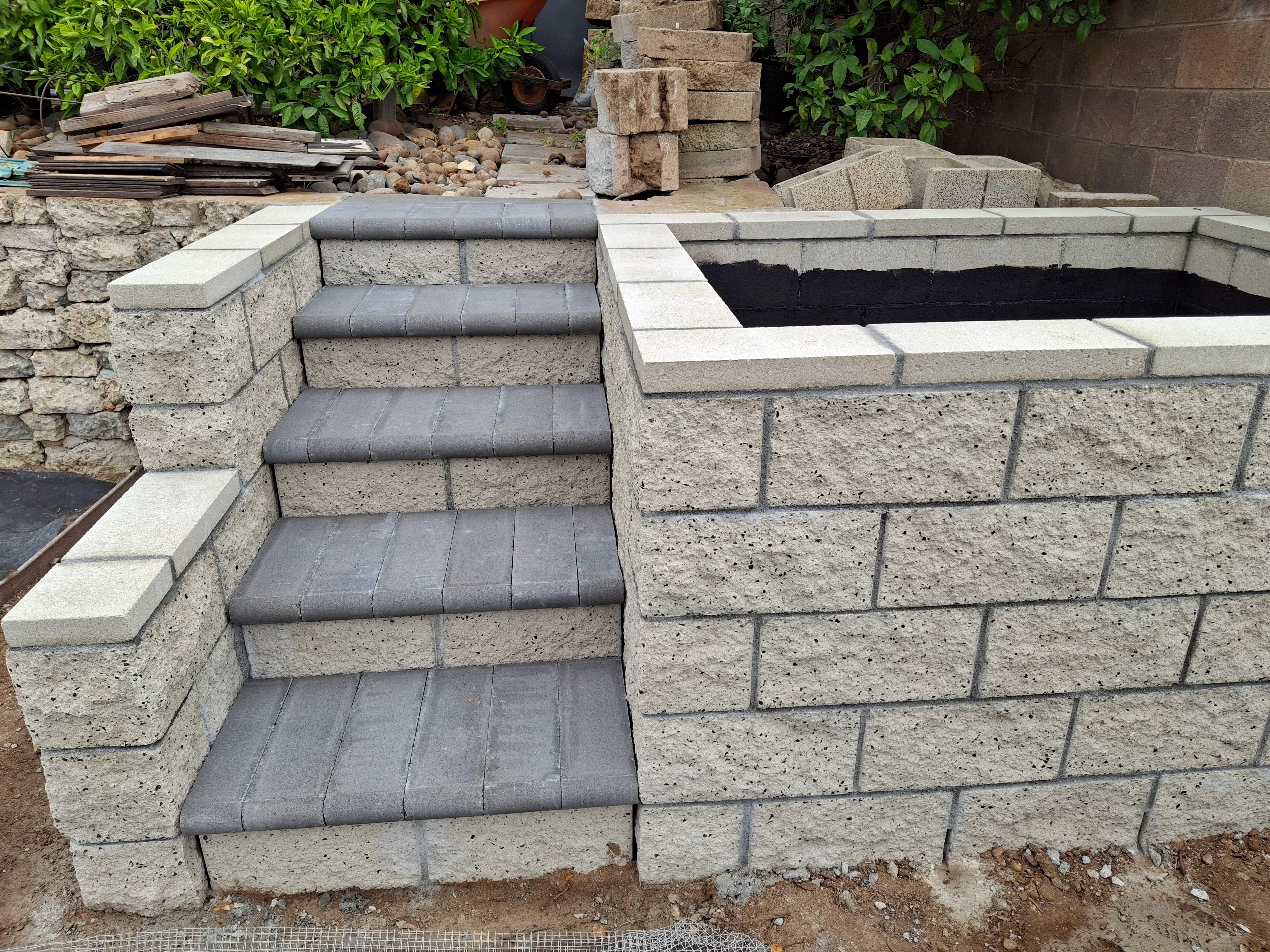 Concrete block retaining wall with dark rubber-treaded steps and finished cap stones