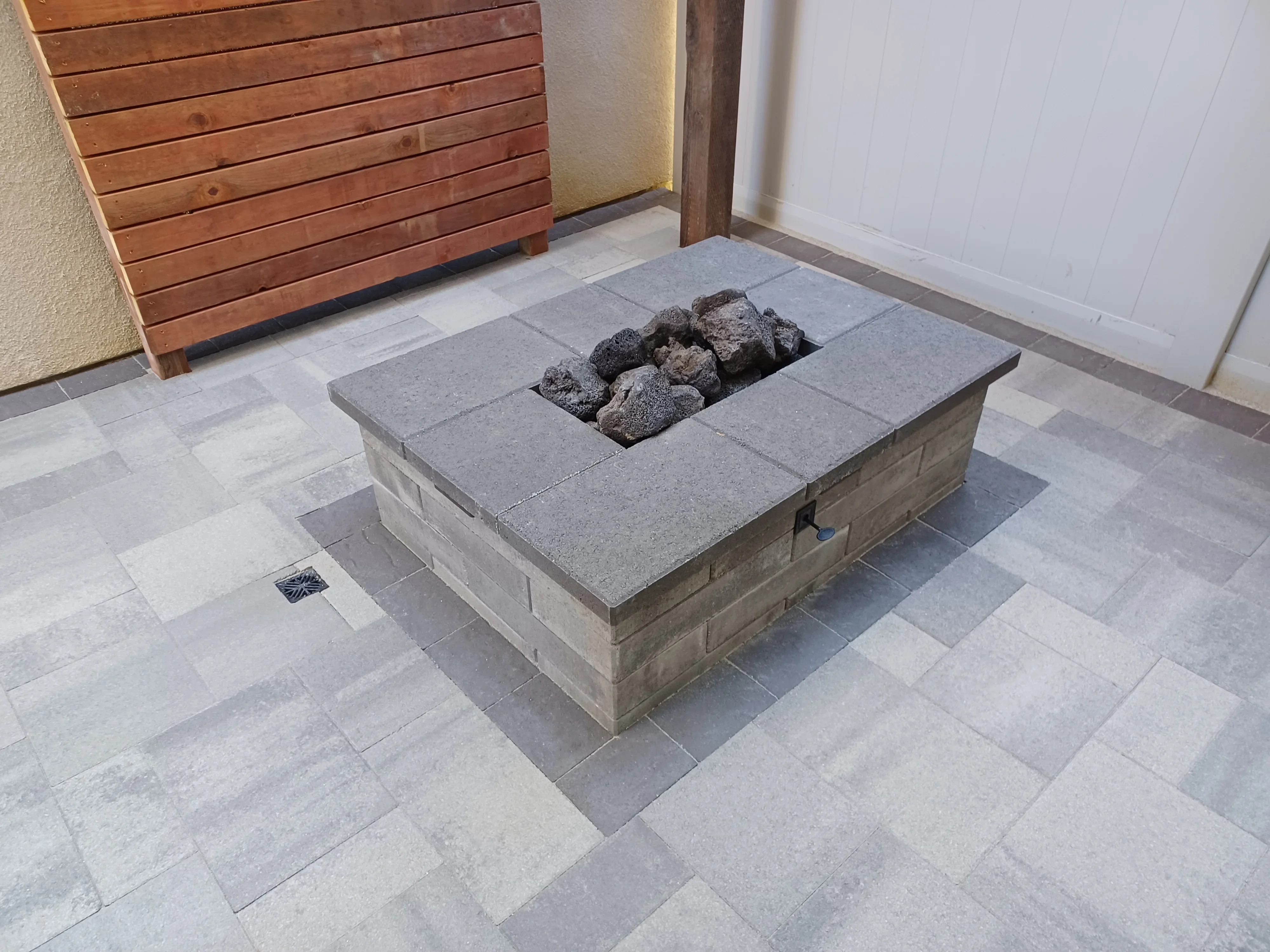 Concrete fire pit with lava rock and removable cap surrounded by geometric concrete pavers