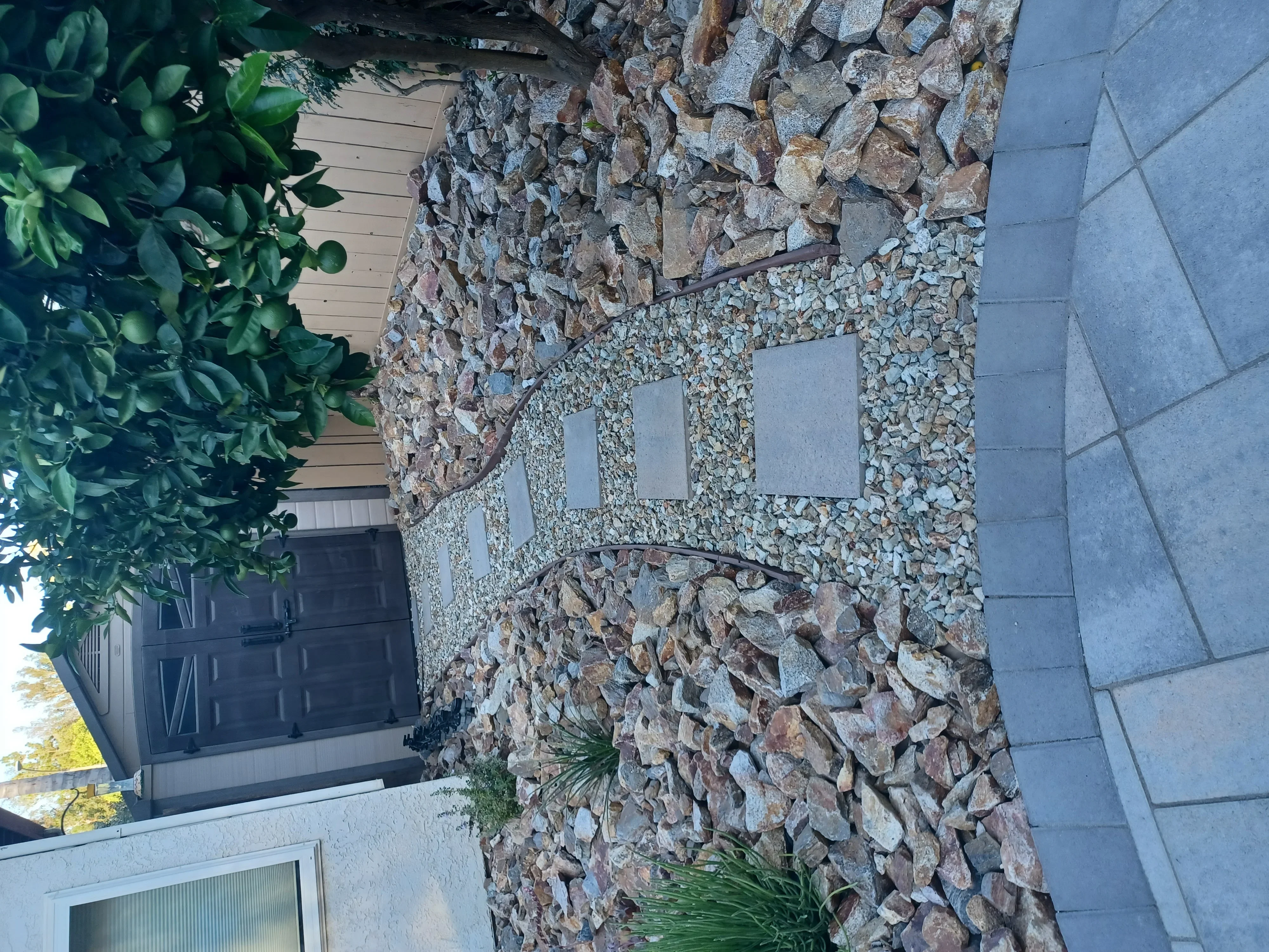 Stacked stone veneer wall with gravel and paver patio, landscaping plants visible