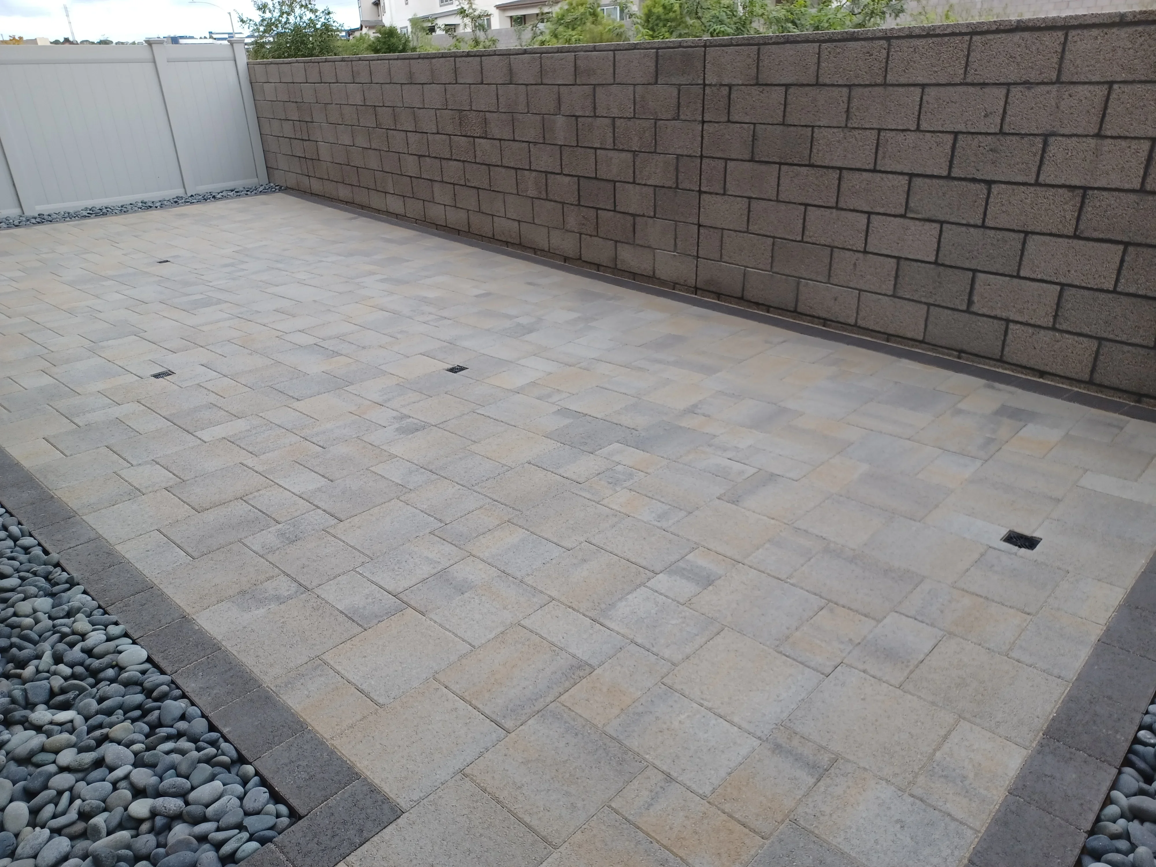 Concrete paver patio in running bond pattern with concrete block retaining wall and river rock drainage border