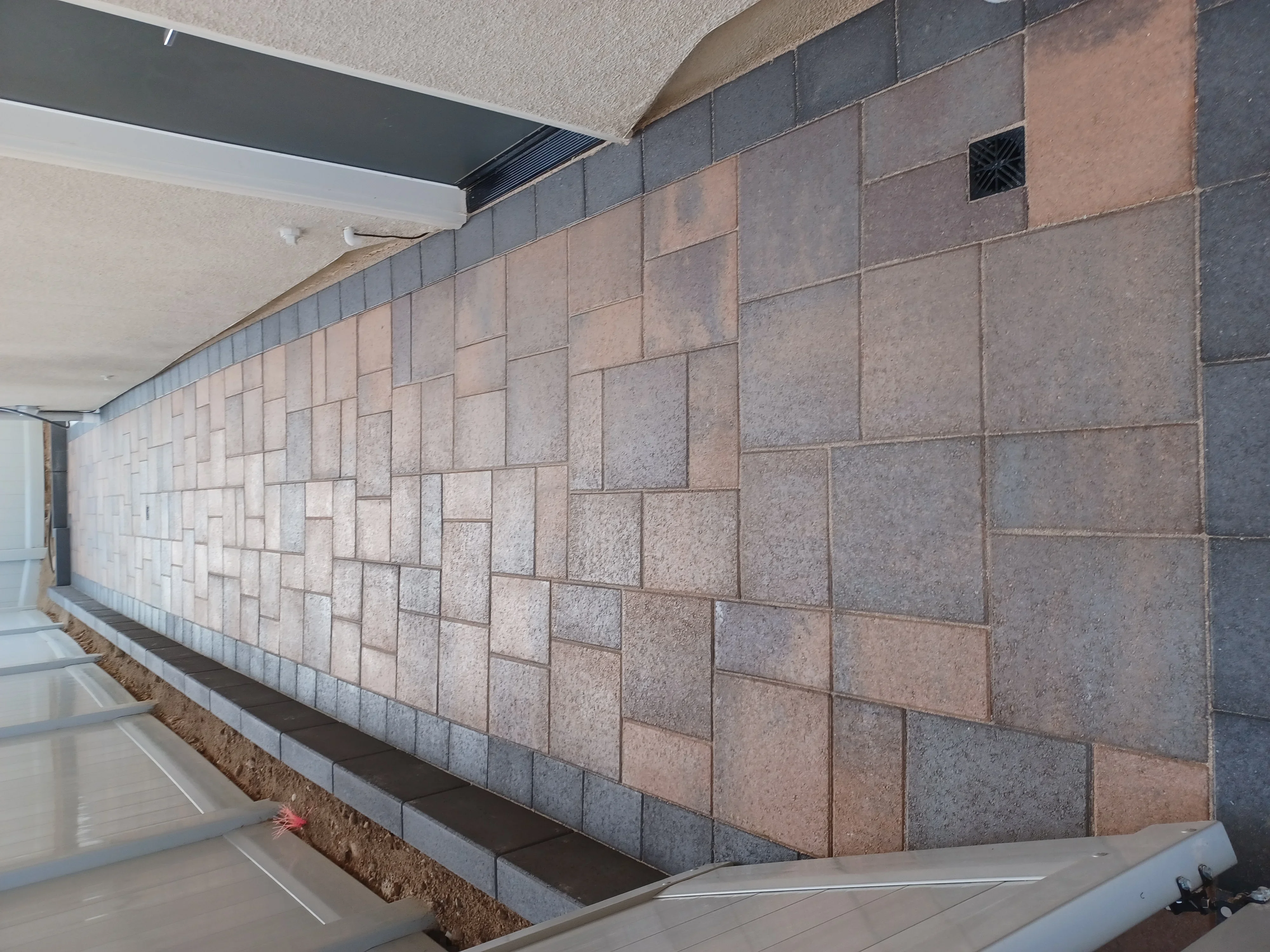 Concrete paver wall with mixed tan and gray tones in running bond pattern with dark cap course
