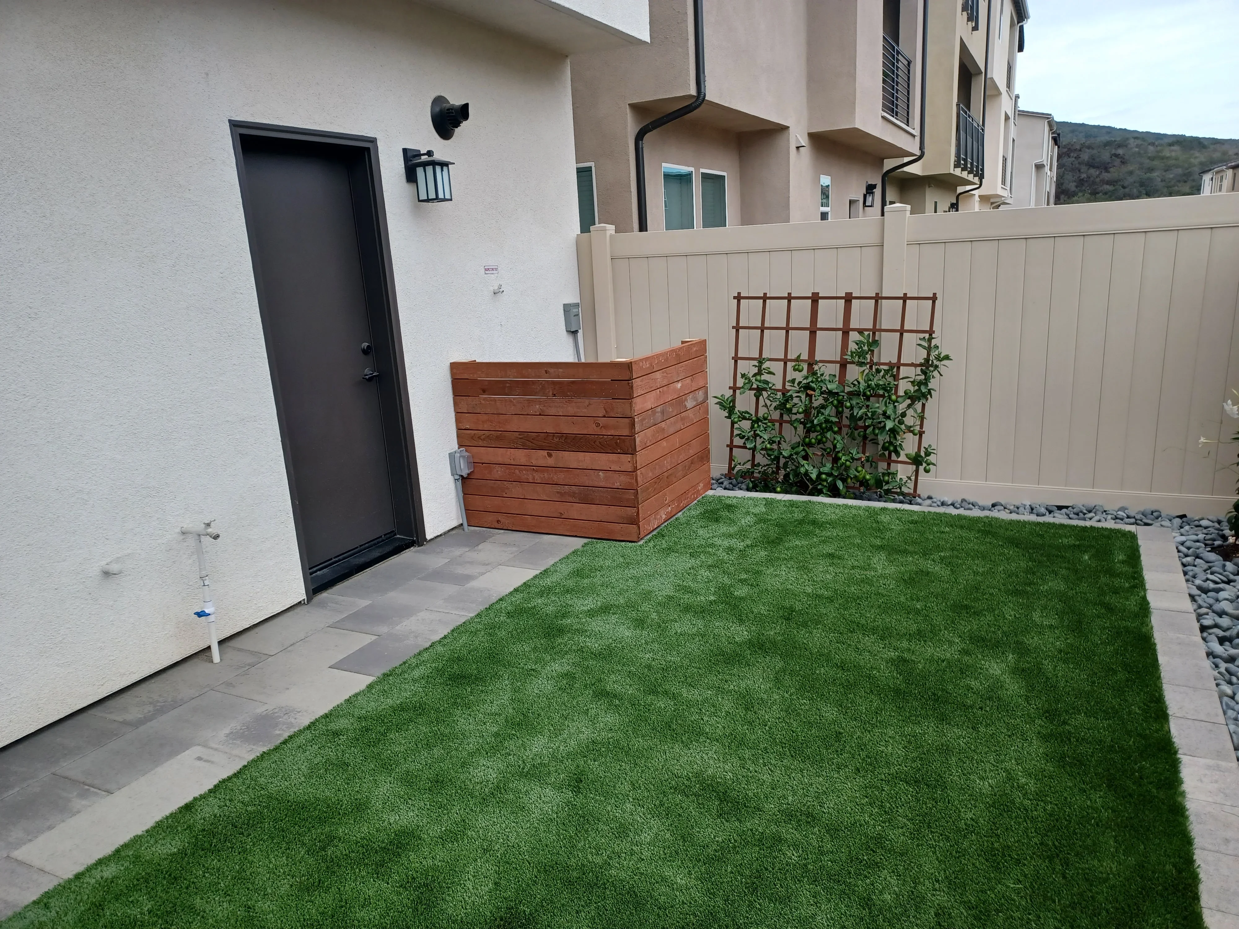 Composite fence, artificial turf, cedar planter with trellis, and gray paver patio in residential courtyard