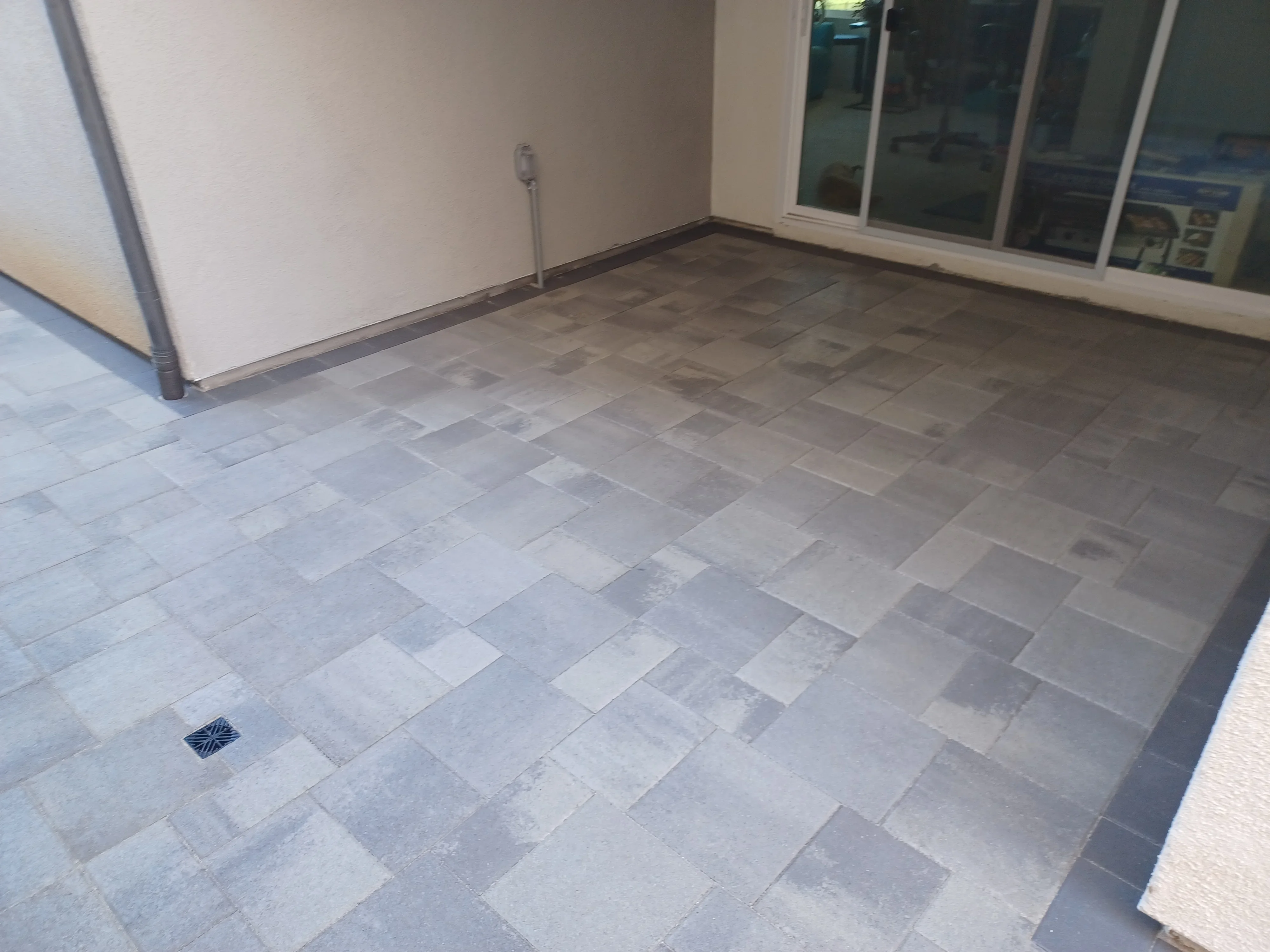 Gray concrete pavers in running bond pattern with metal edging and drainage basin