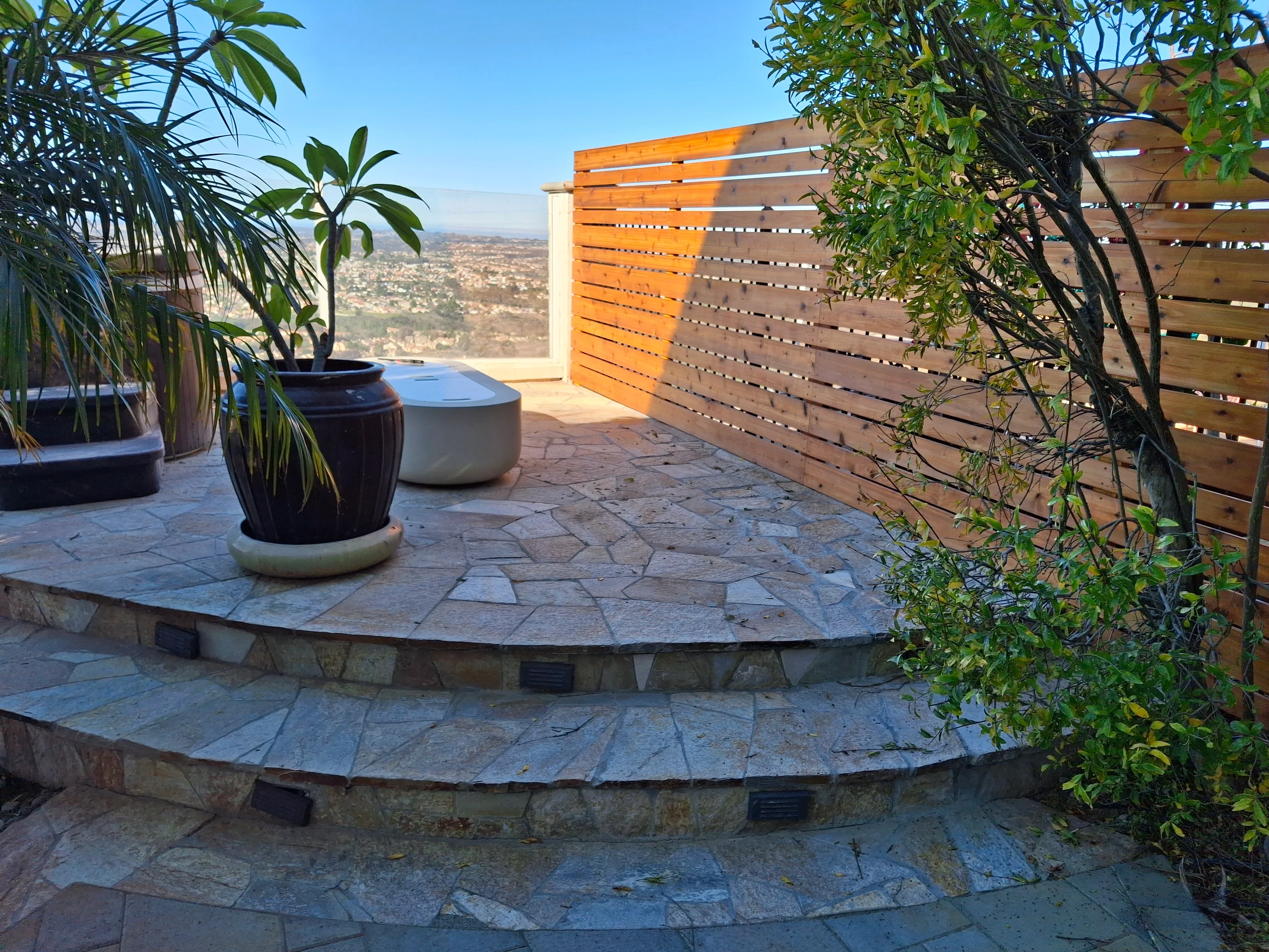 Circular flagstone patio with stone seating wall, wood privacy screen, and container plantings