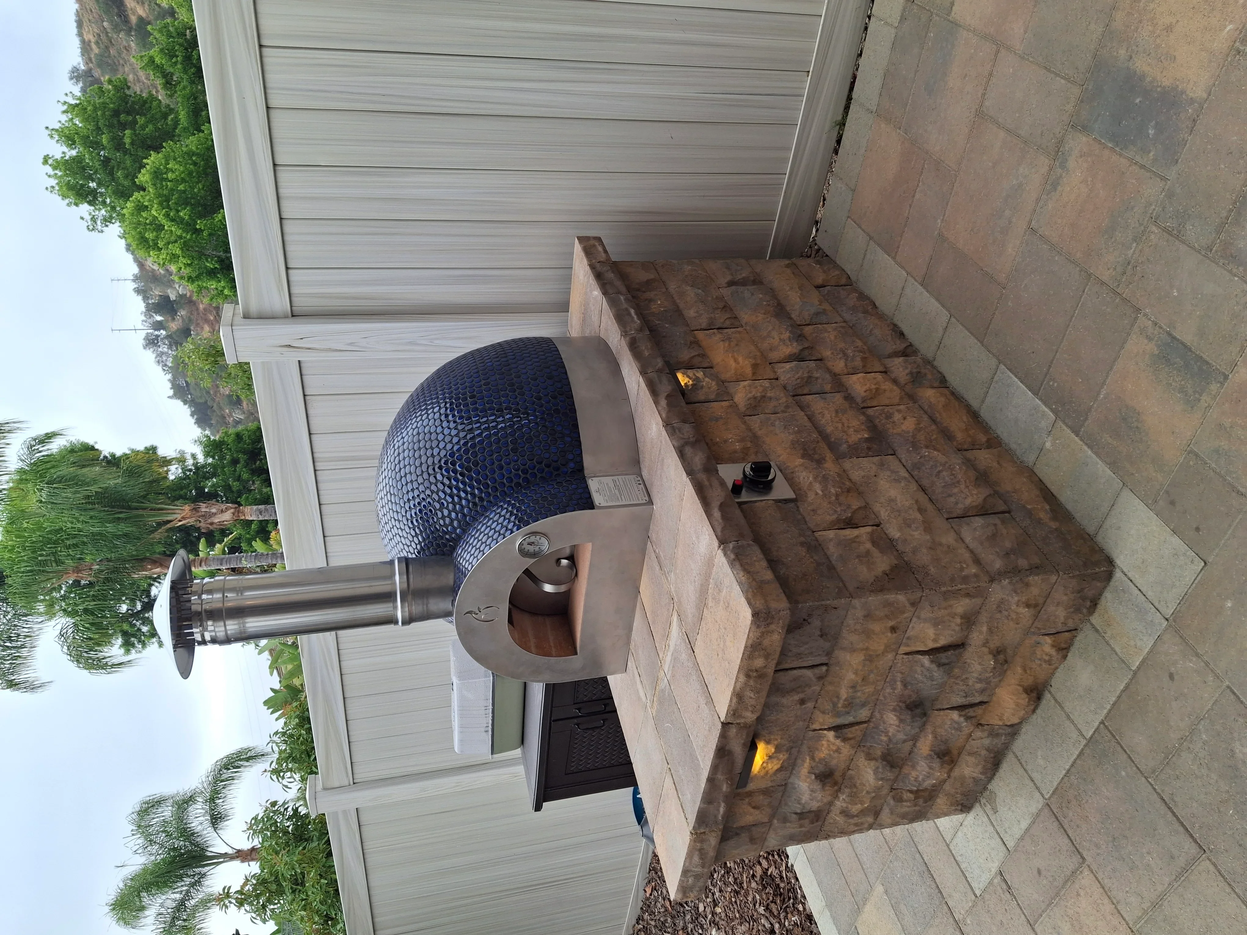 Brick outdoor fireplace with steel chimney on concrete paver patio