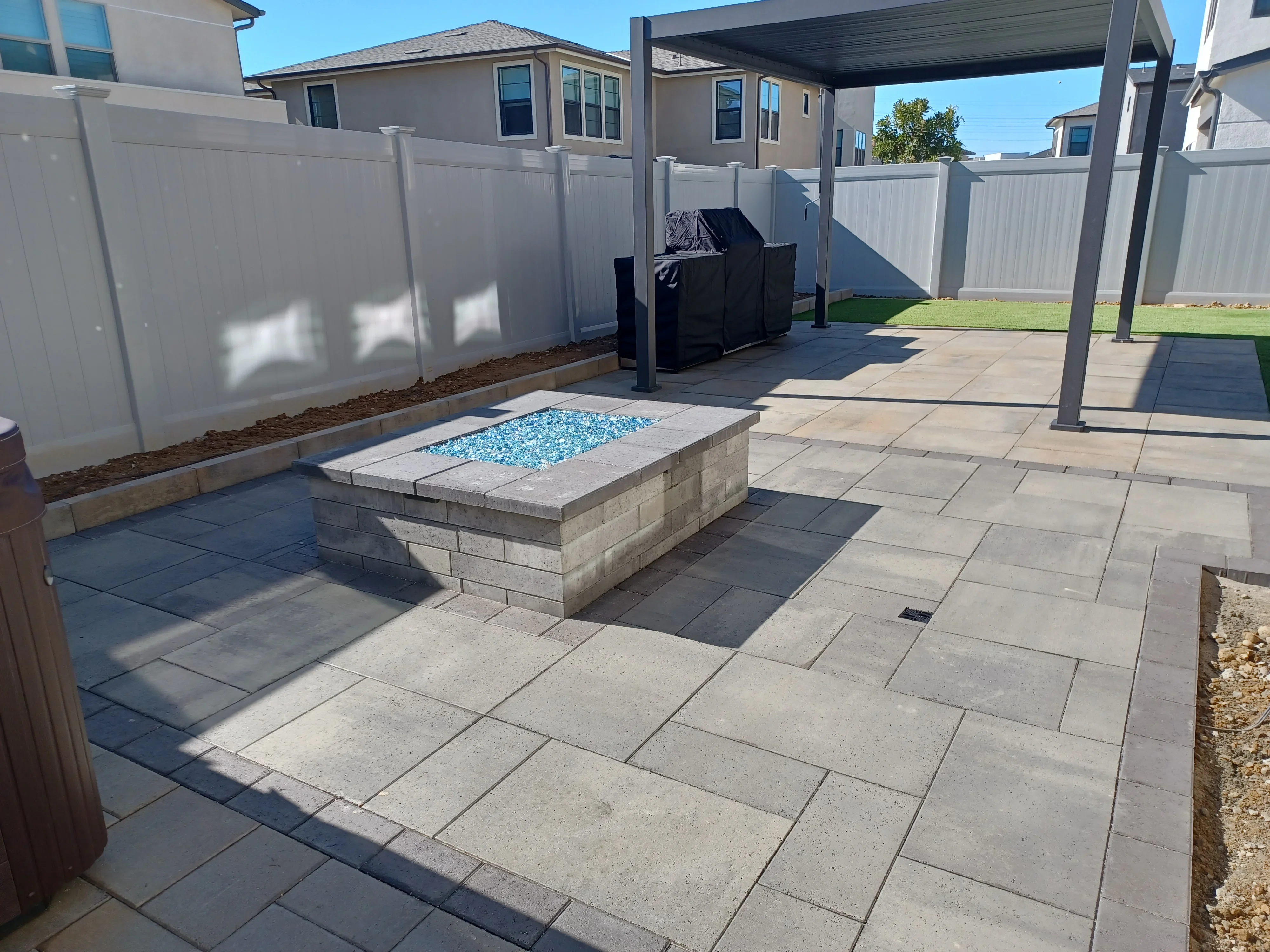 Concrete paver patio with built-in fire pit, steel pergola, and vinyl privacy fencing