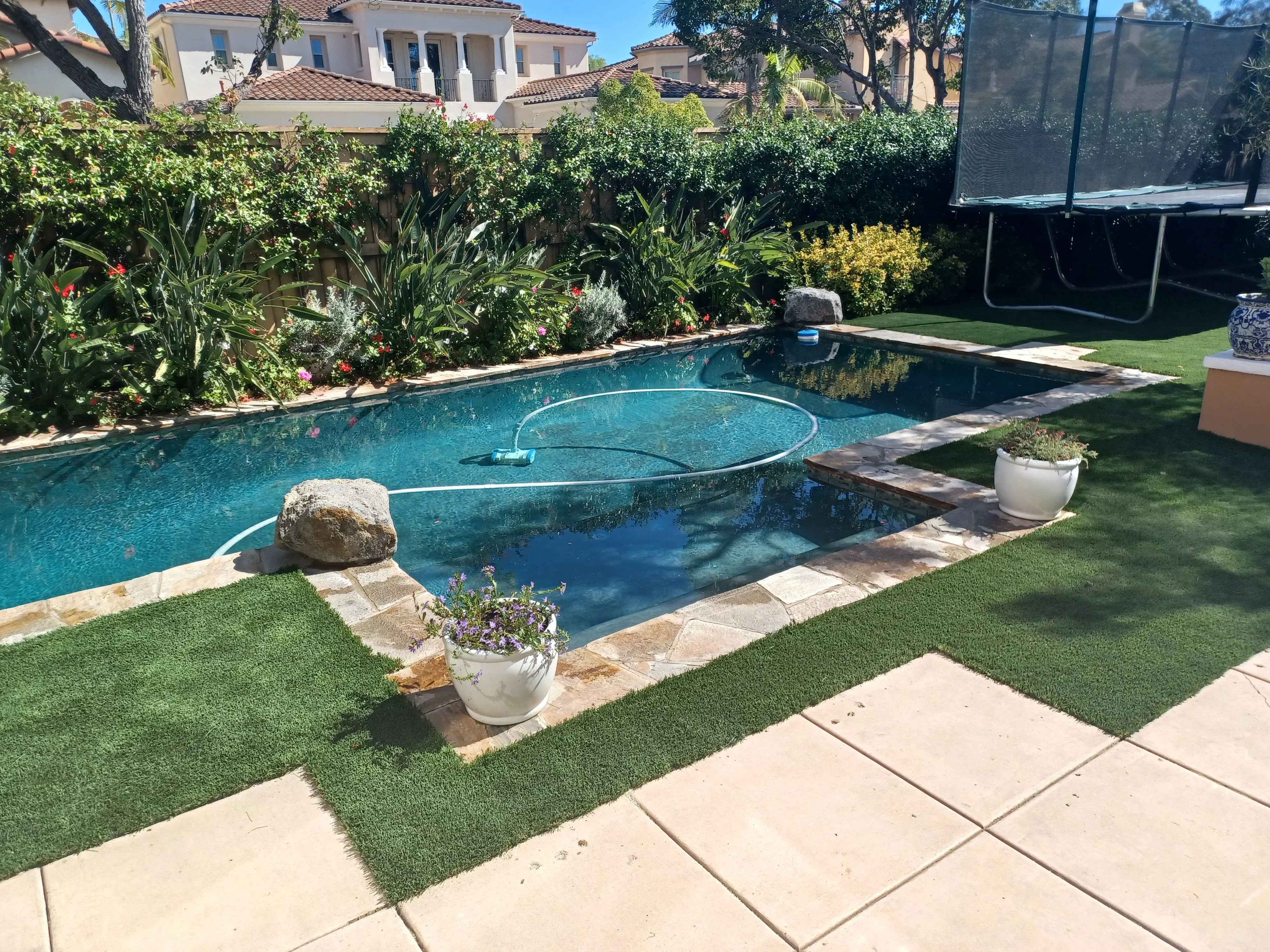 Travertine pool deck with geometric pavers, stone coping, and decorative boulders surrounding resort-style pool