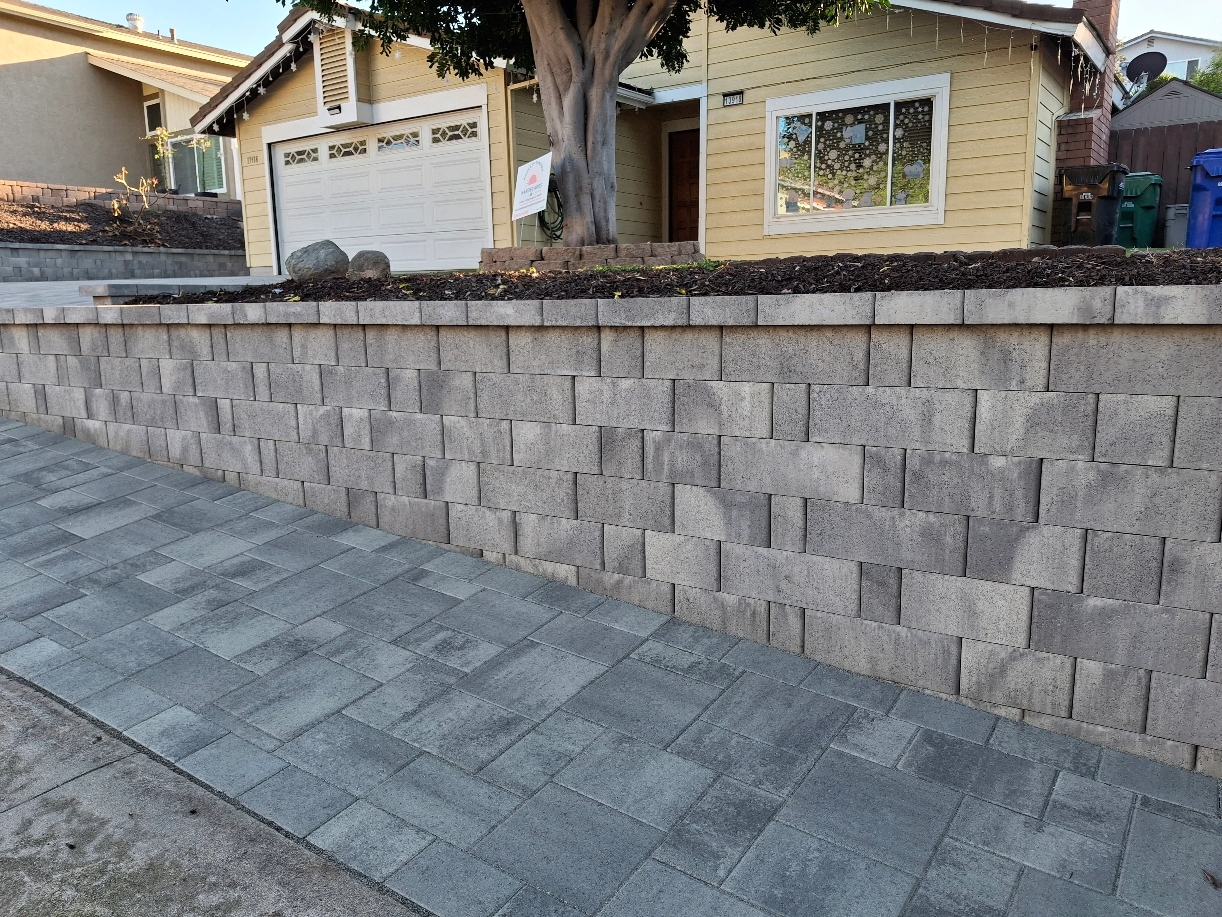 Gray concrete block retaining wall with stacked paver patio in front of residential home