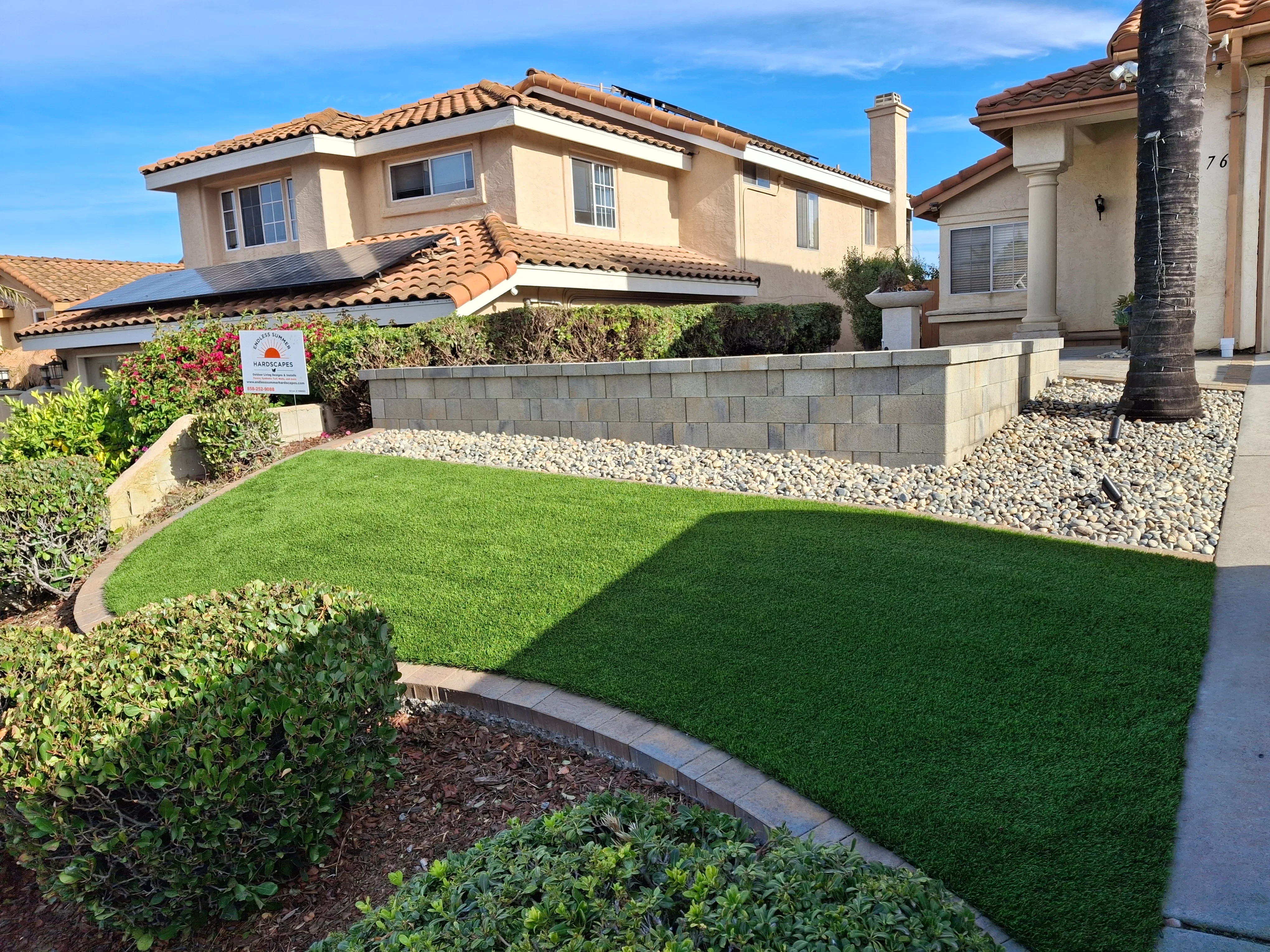 Concrete block retaining wall with new sod lawn, river rock, and planted shrub beds