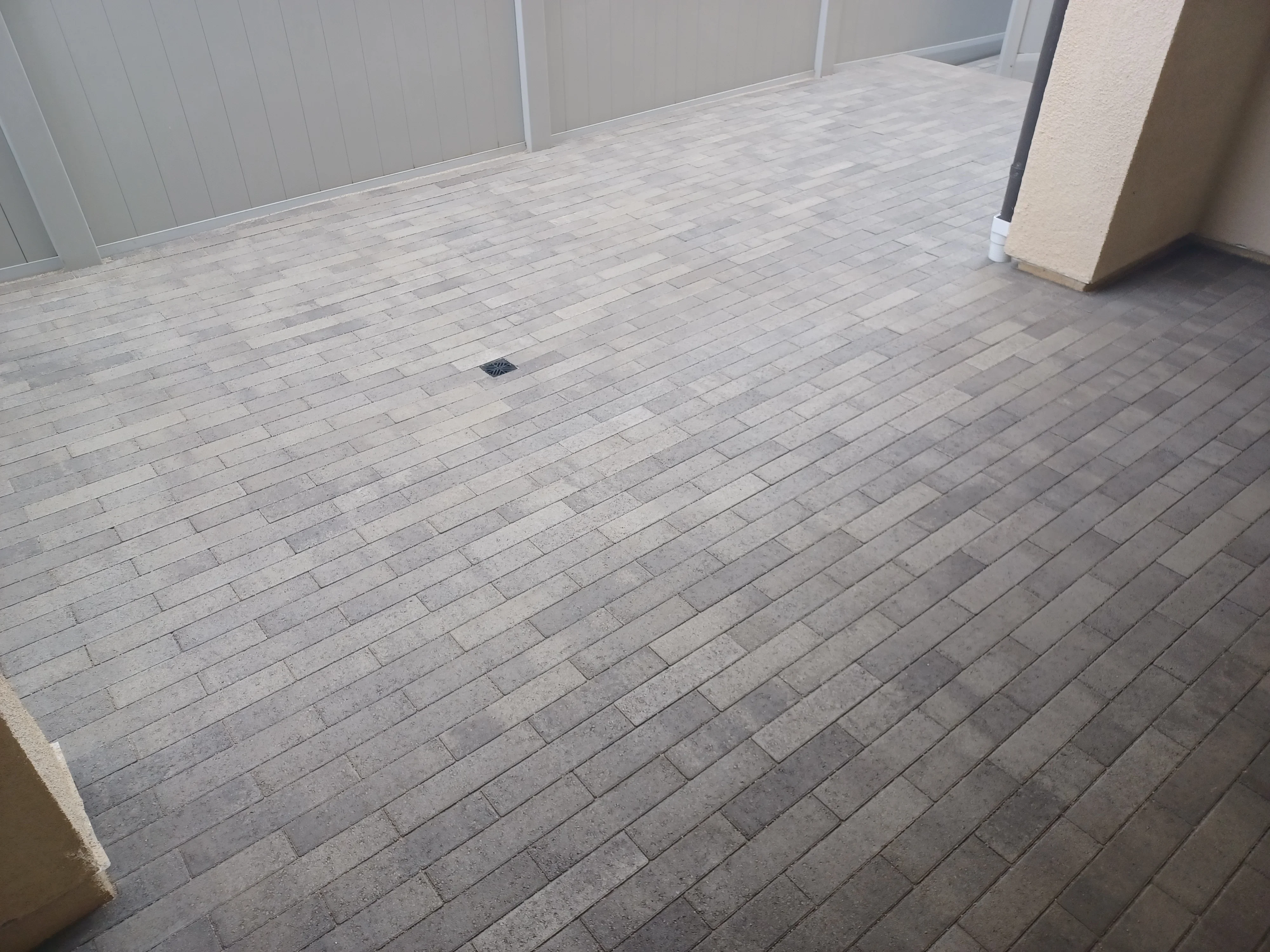 Light gray permeable pavers in running bond pattern with drainage inlet and finished edges