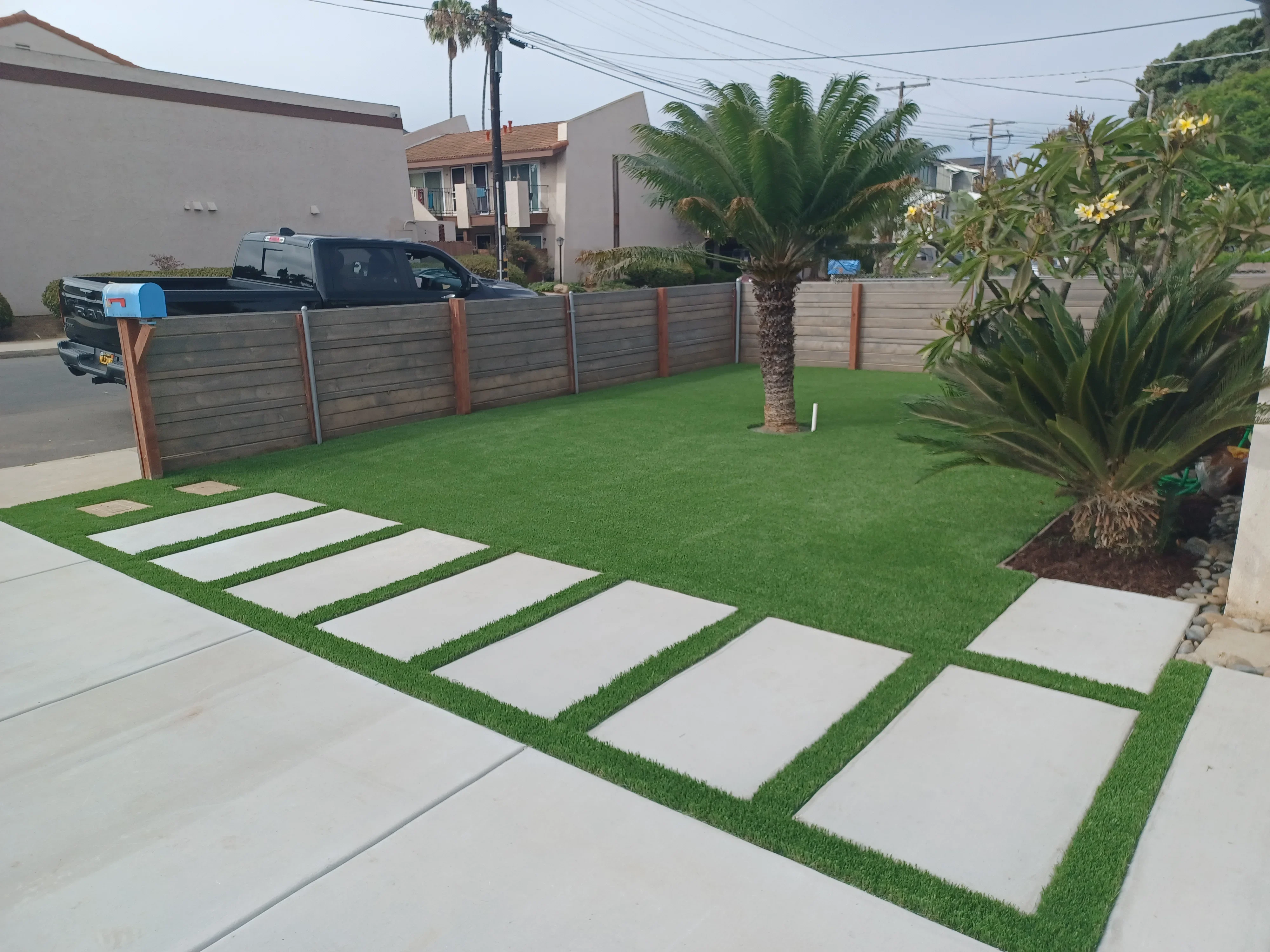 Concrete pavers in synthetic turf with horizontal wood fence and tropical plants