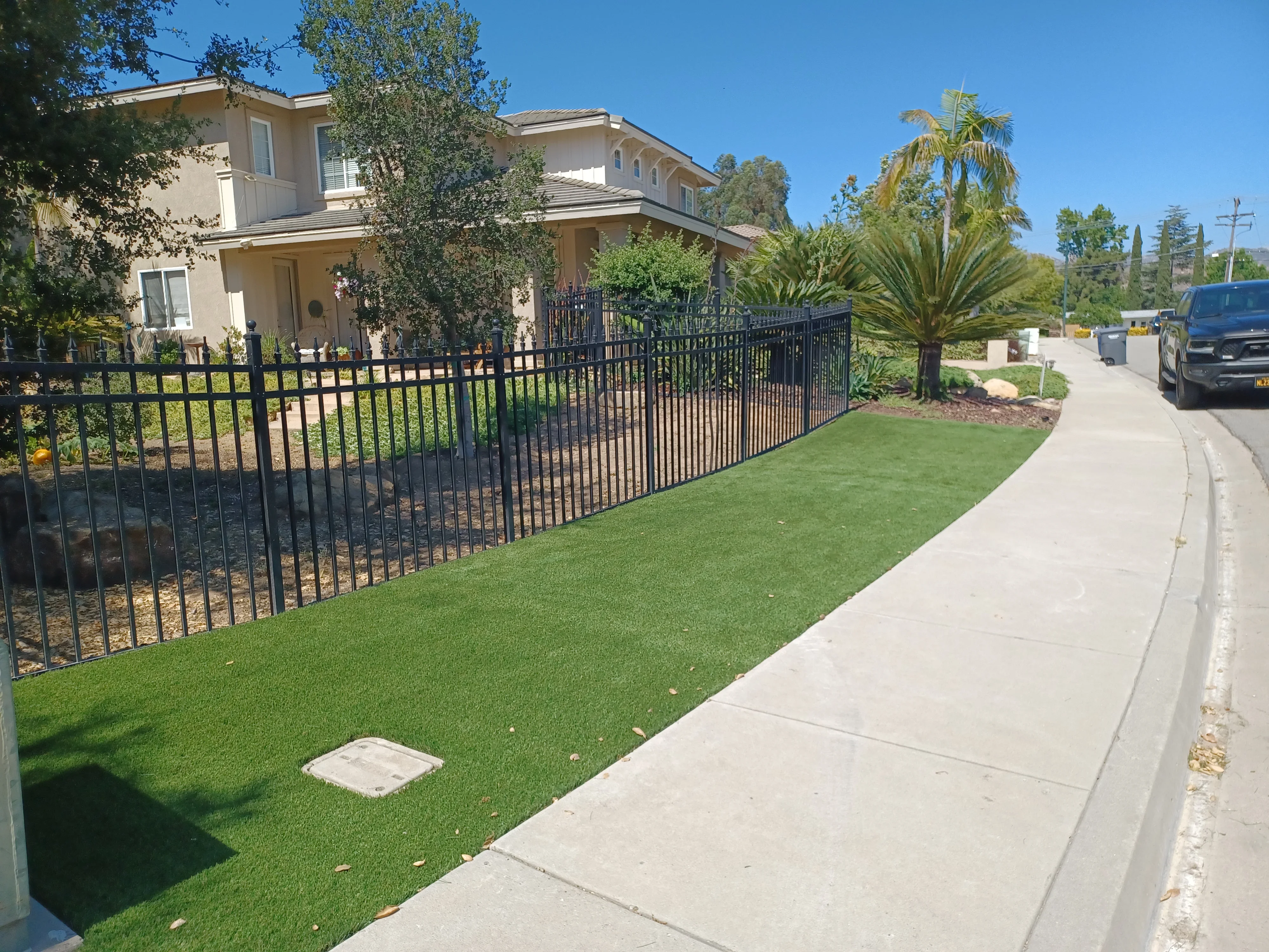 Black aluminum fence with synthetic turf lawn and concrete sidewalk along residential property