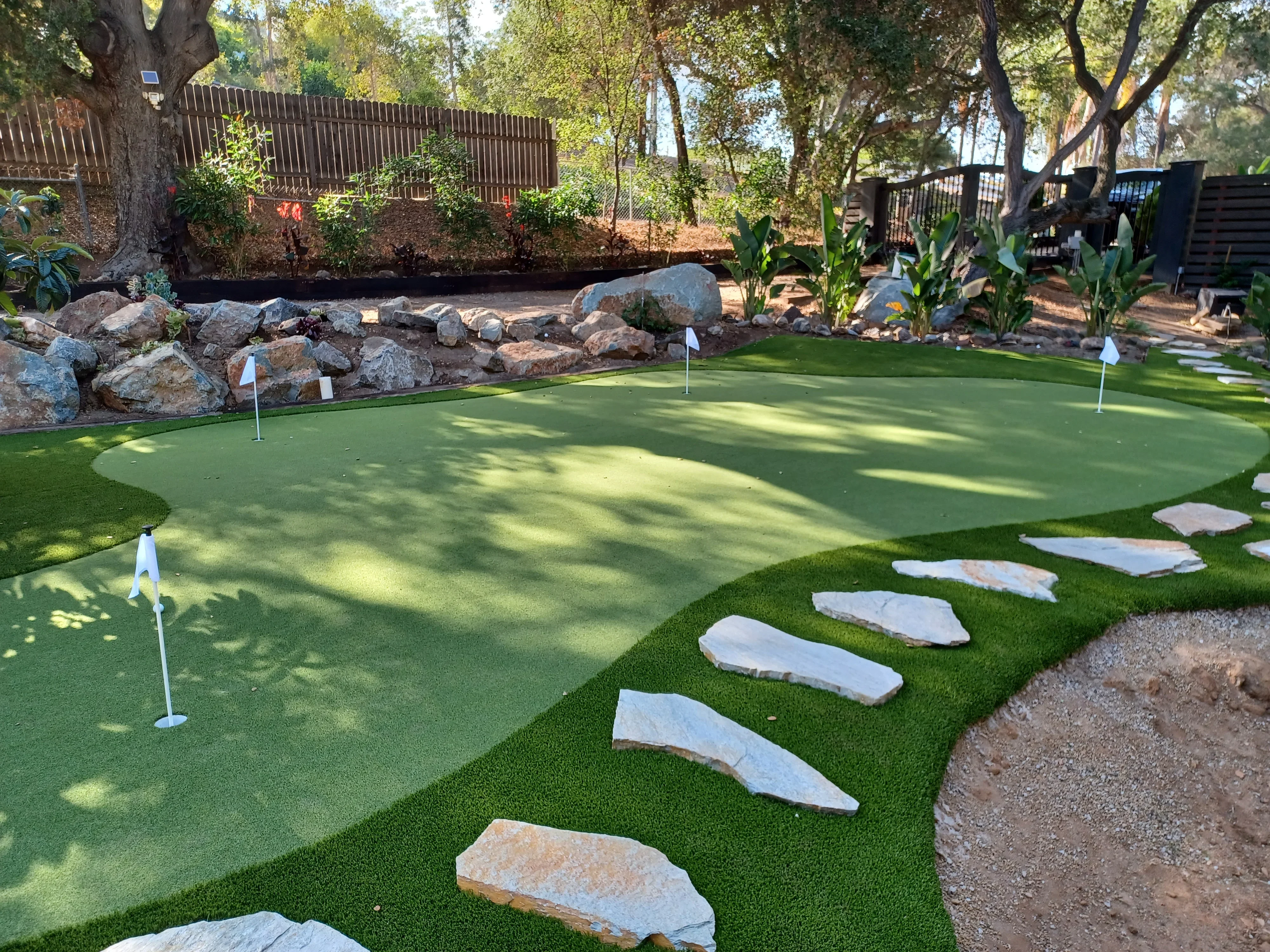 Synthetic putting green with stone steppers, boulder wall, and manicured landscape edging