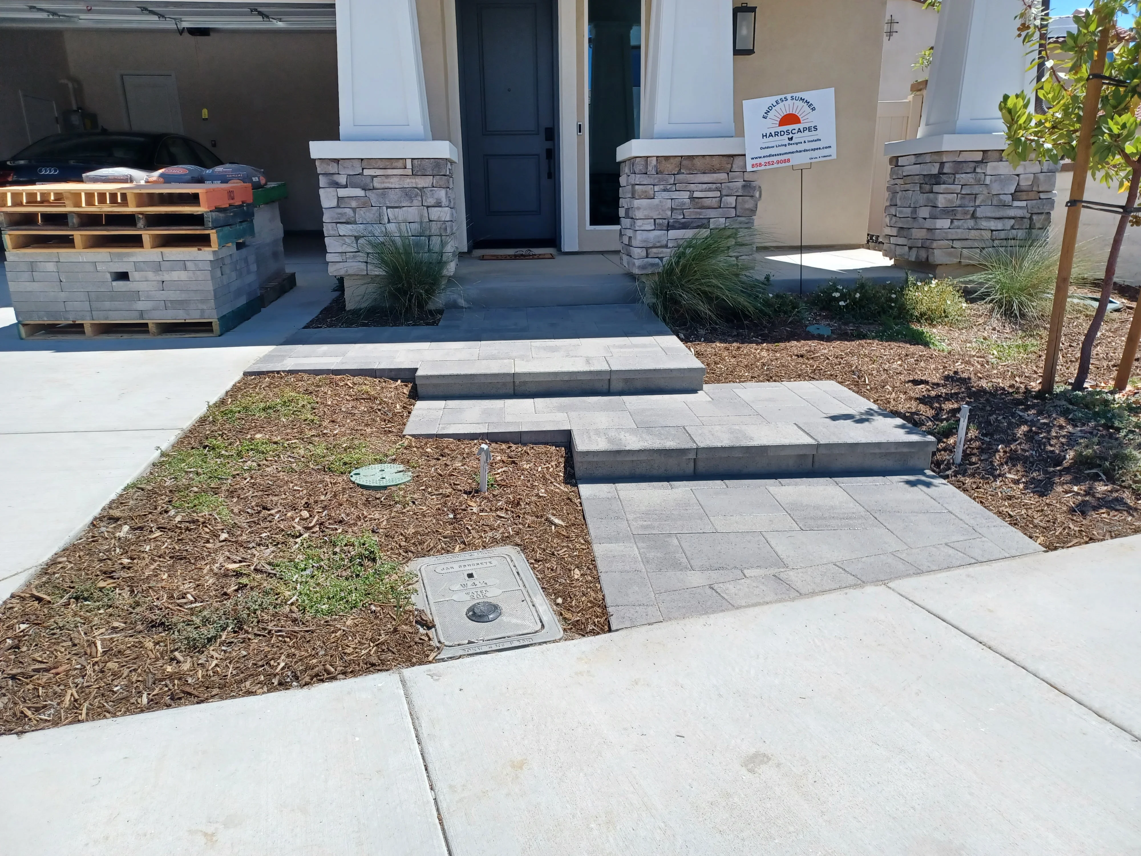 Permeable paver walkway with stone pillar columns, mulch beds, and ornamental grasses