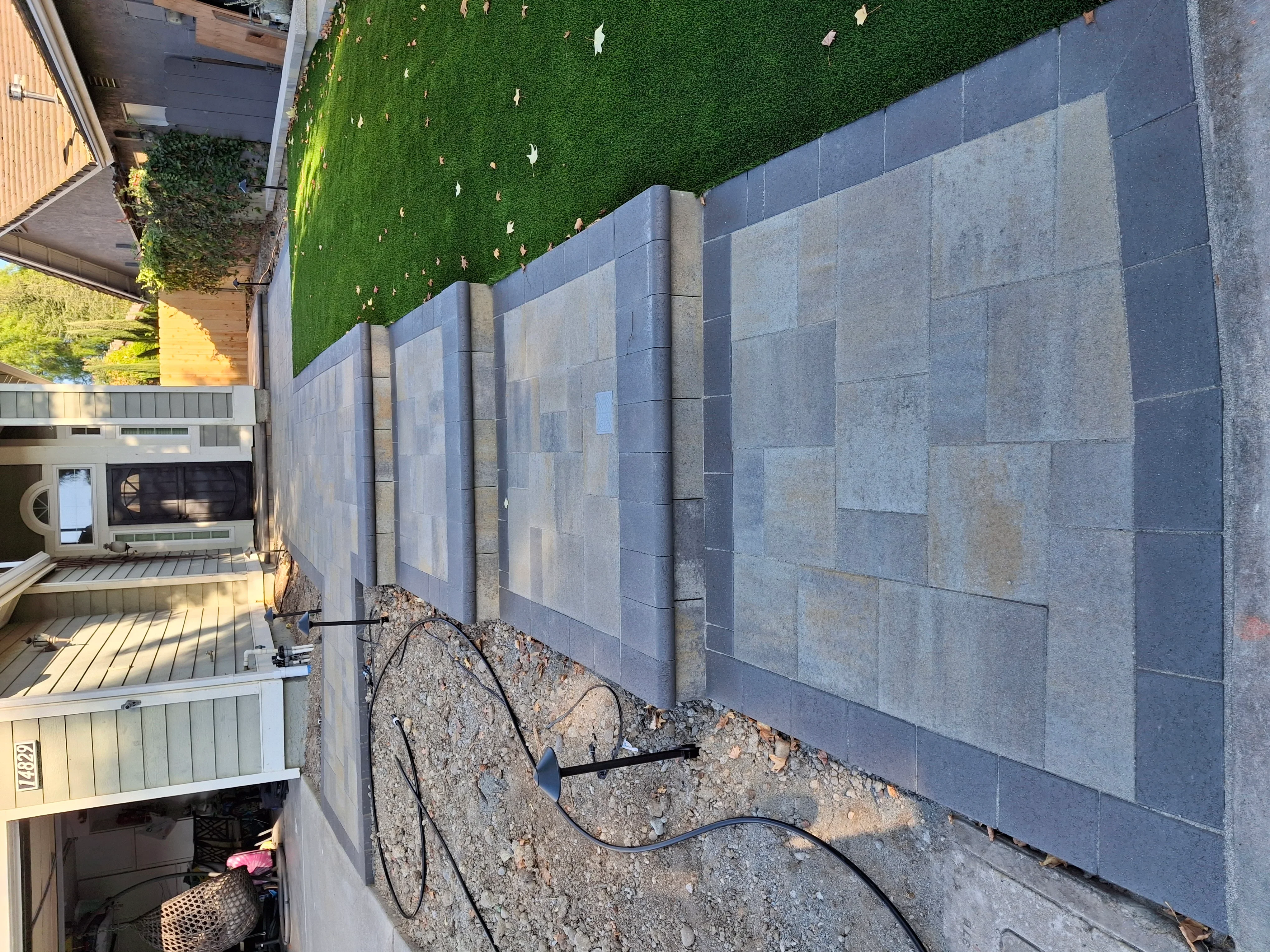 Gray segmental retaining wall with artificial turf cap and gravel base drainage