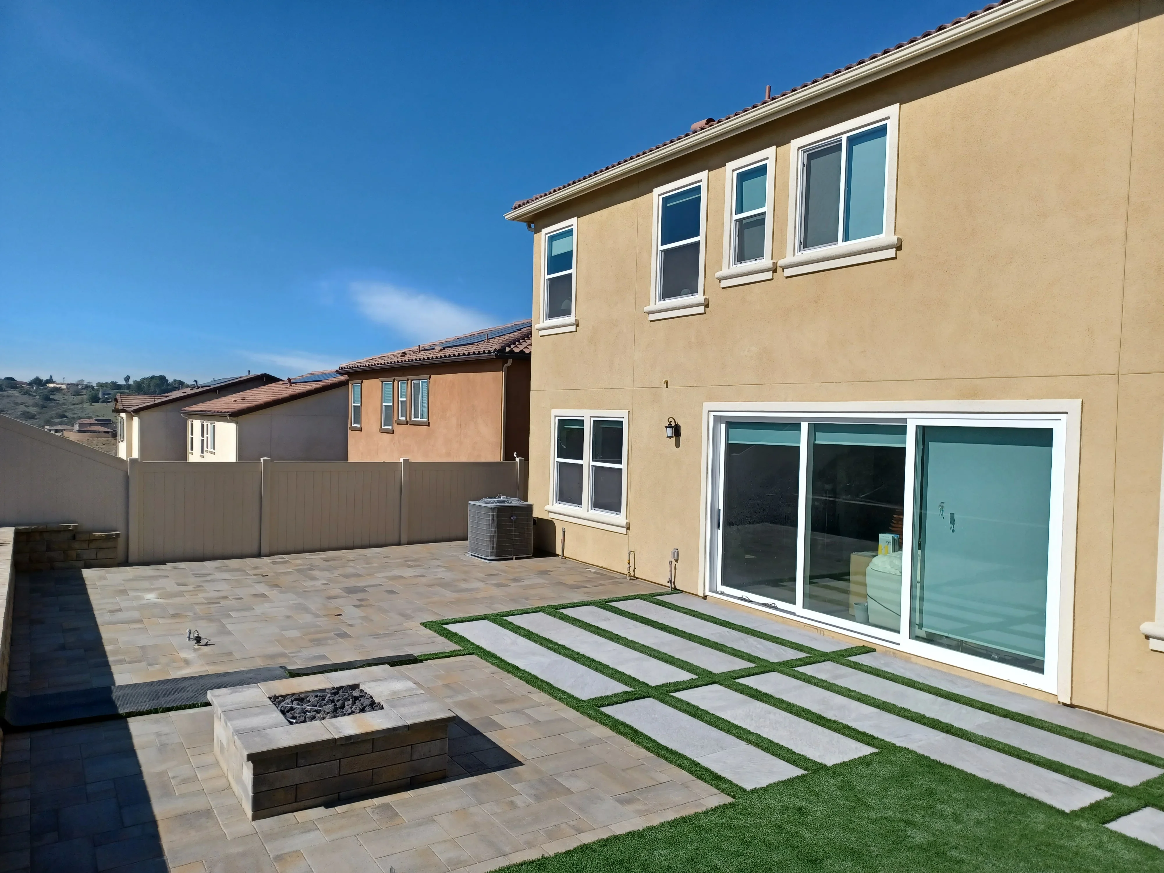 Paver patio with stepping stones, synthetic turf, and stone fire pit in backyard