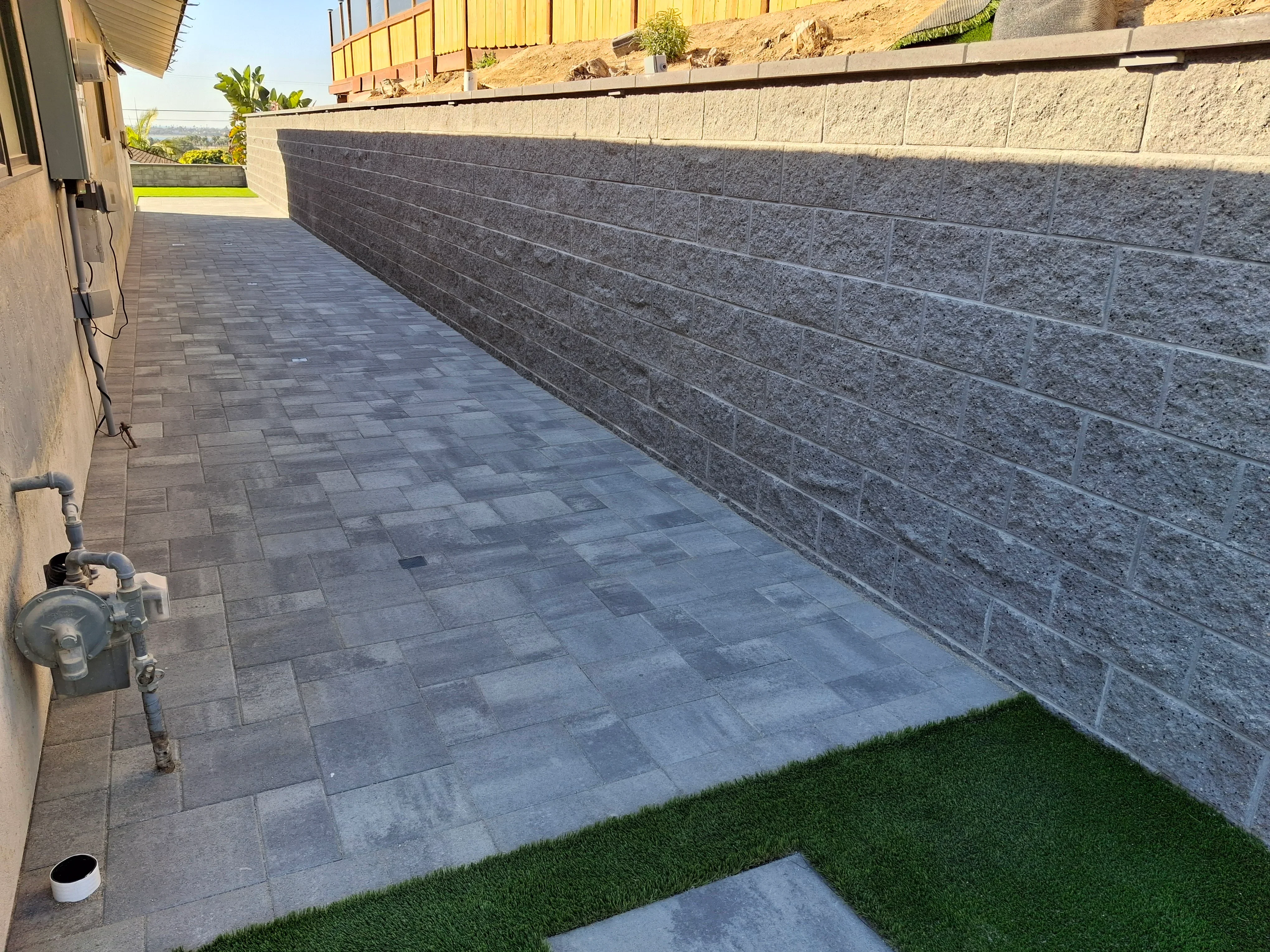 Curved gray block retaining wall with geometric paver patio and drainage system