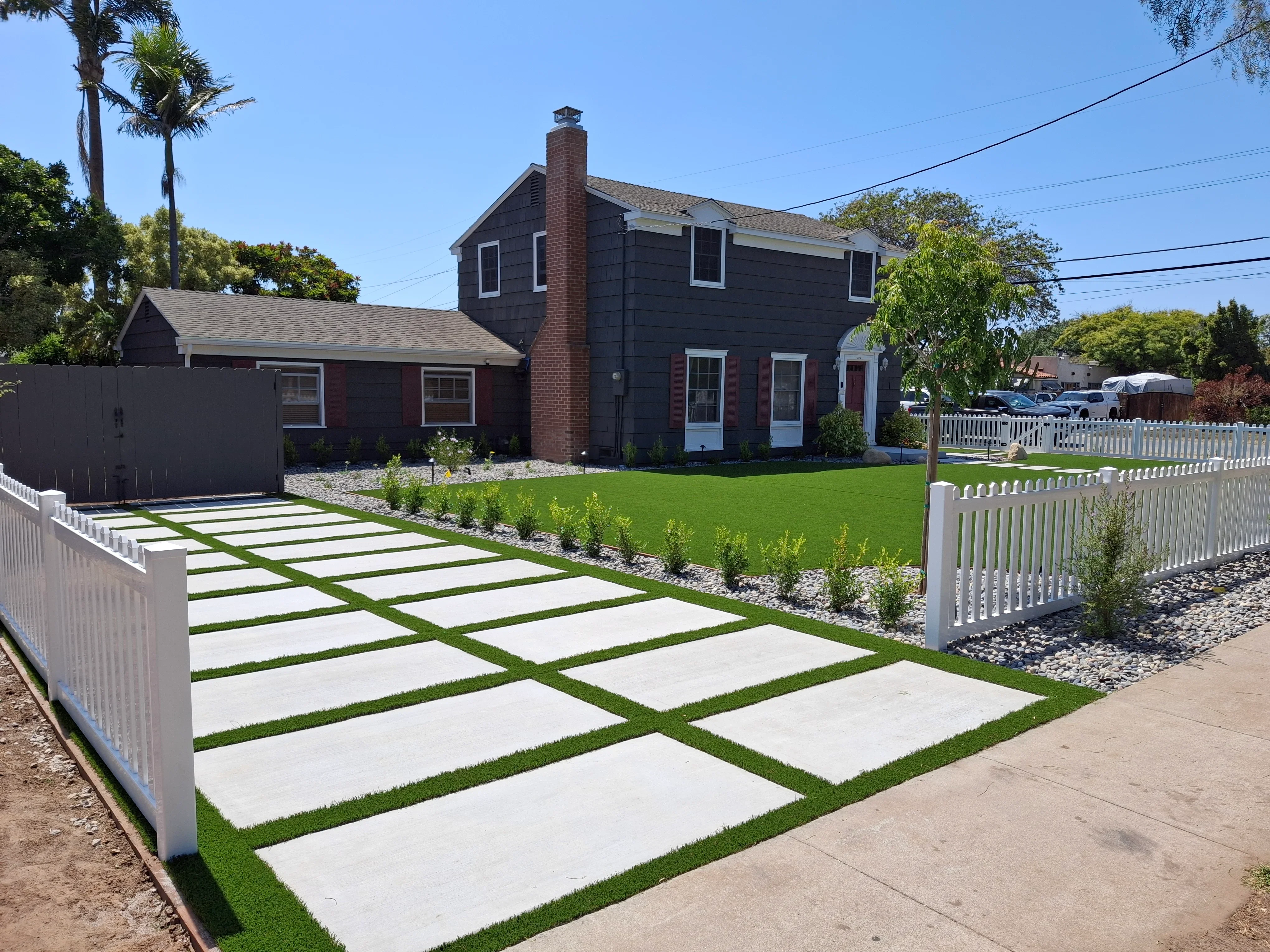 Concrete pavers with grass strips, white vinyl fence, gravel borders, and landscape plantings