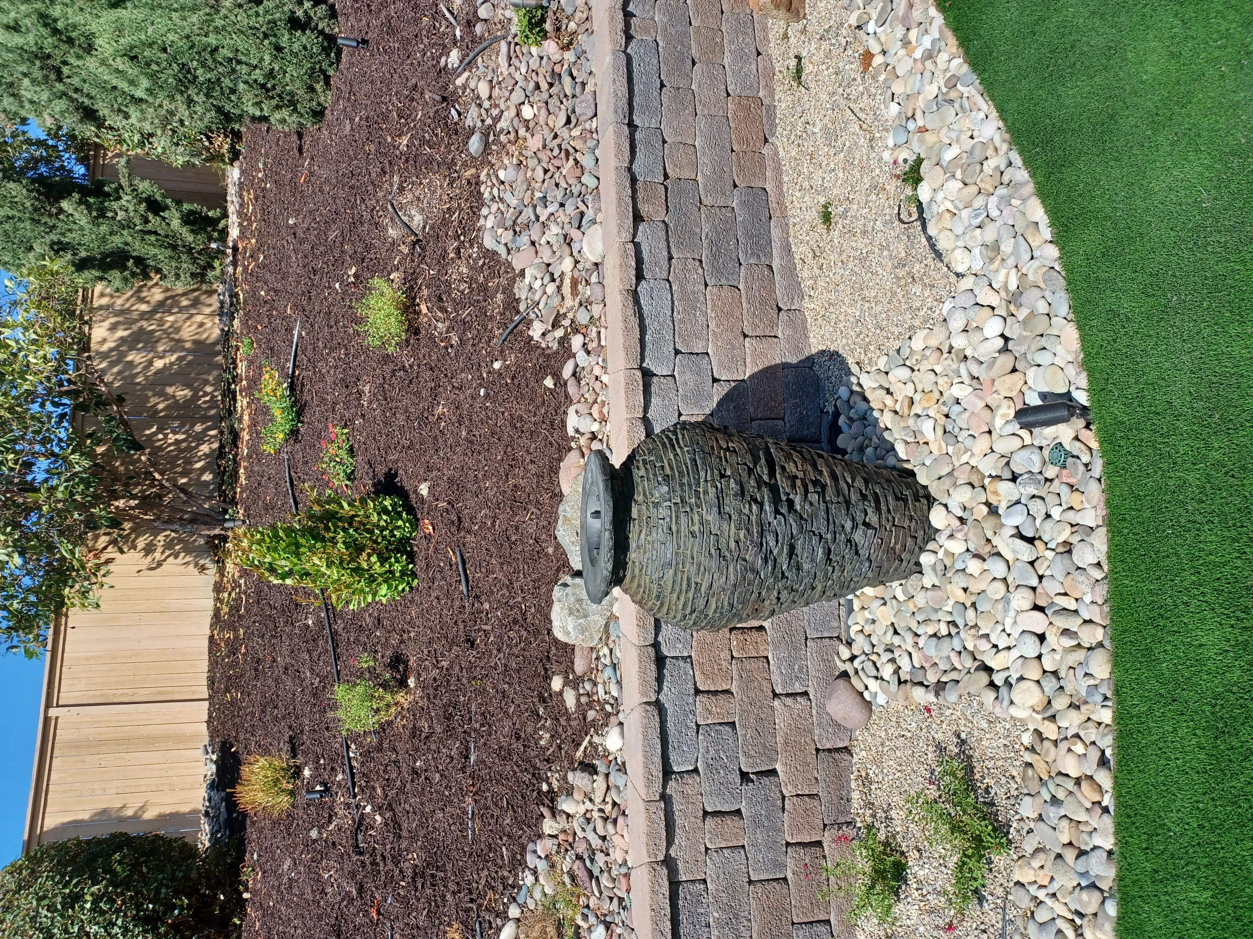 Gray permeable pavers, white river rock, tan gravel, and mulch hardscape with urn planter