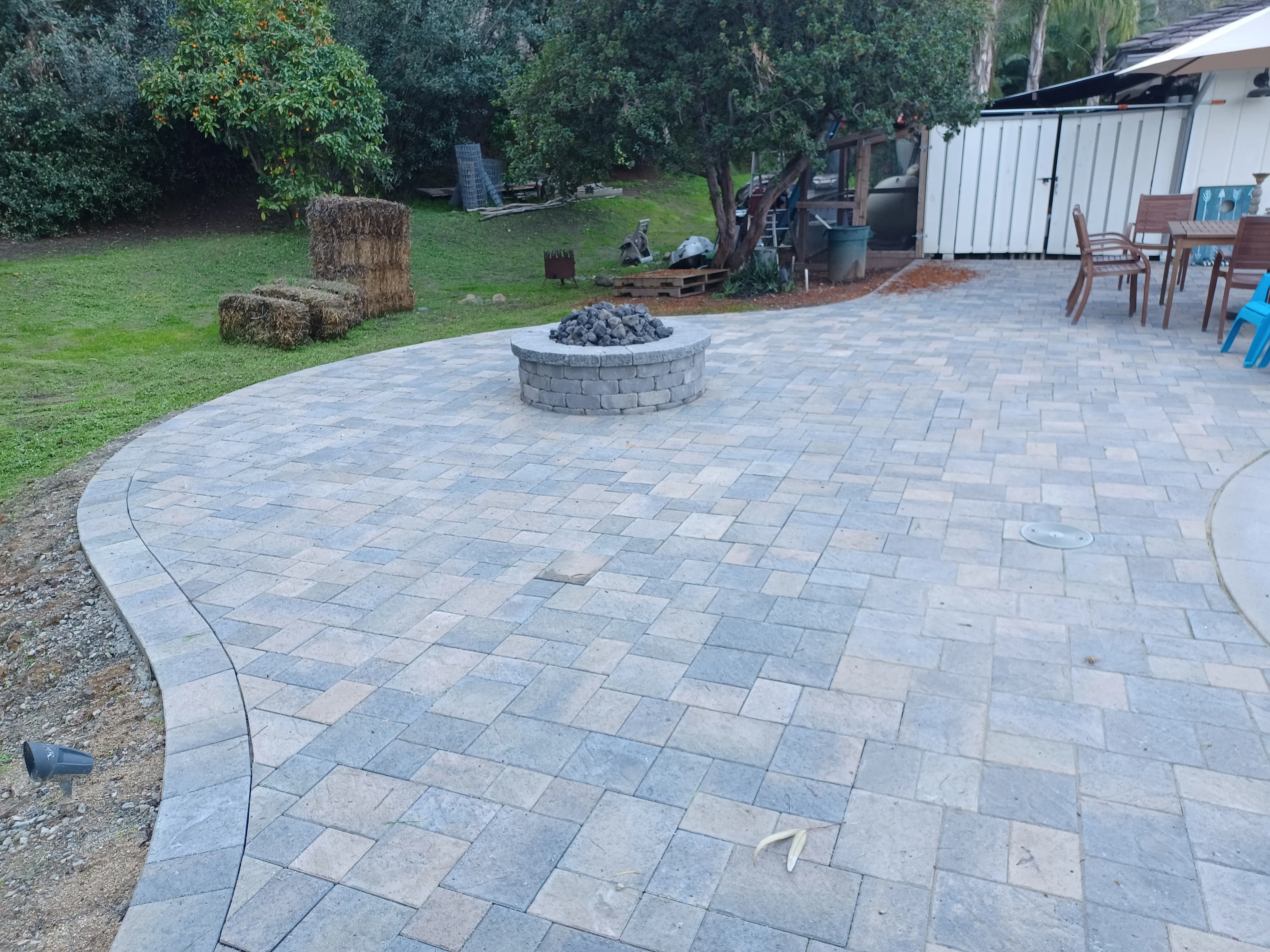 Curved paver patio with herringbone pattern and circular fire pit surrounded by lawn and landscaping