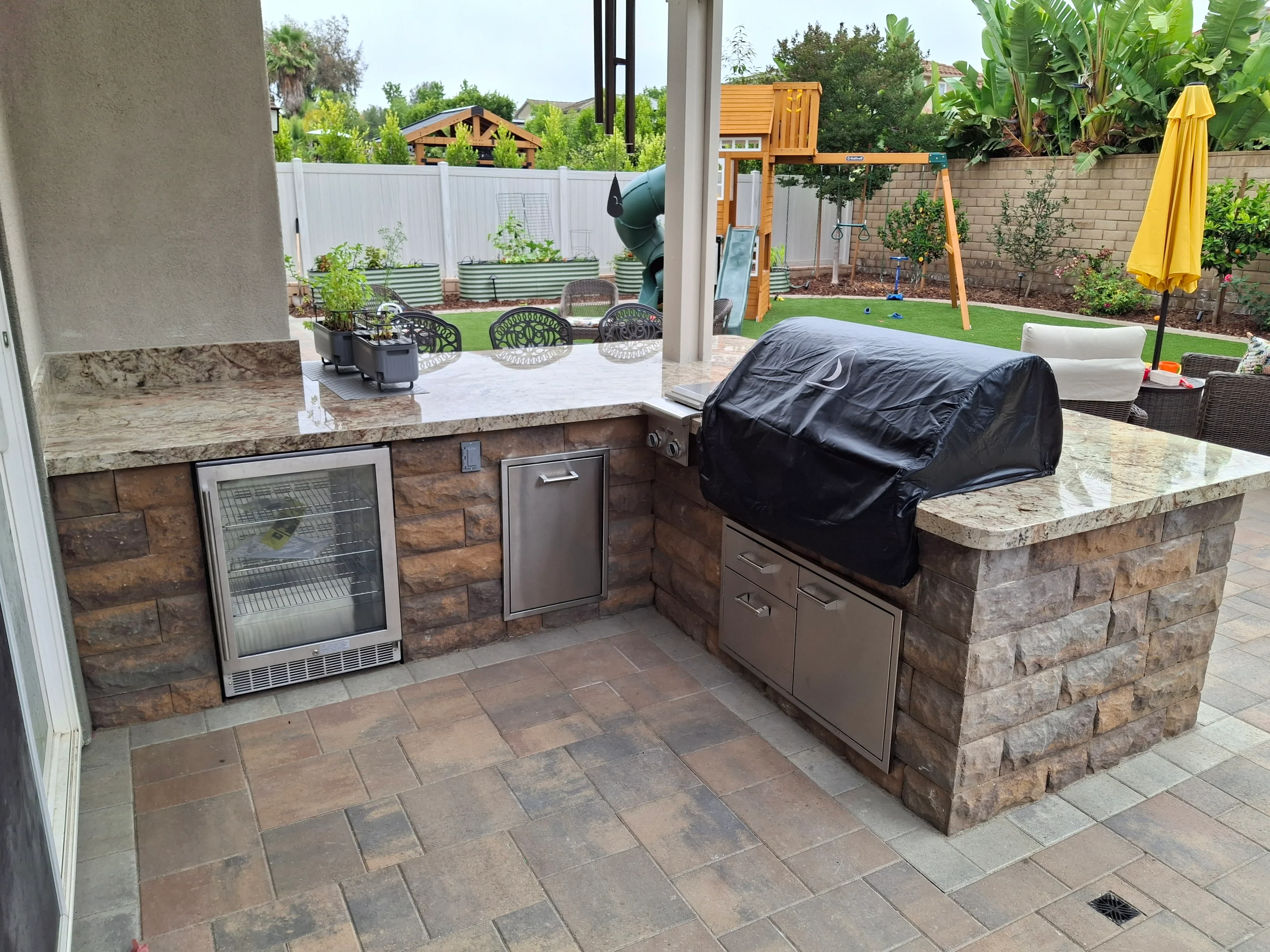 Stacked stone outdoor kitchen with granite counters, built-in grill, and paver patio