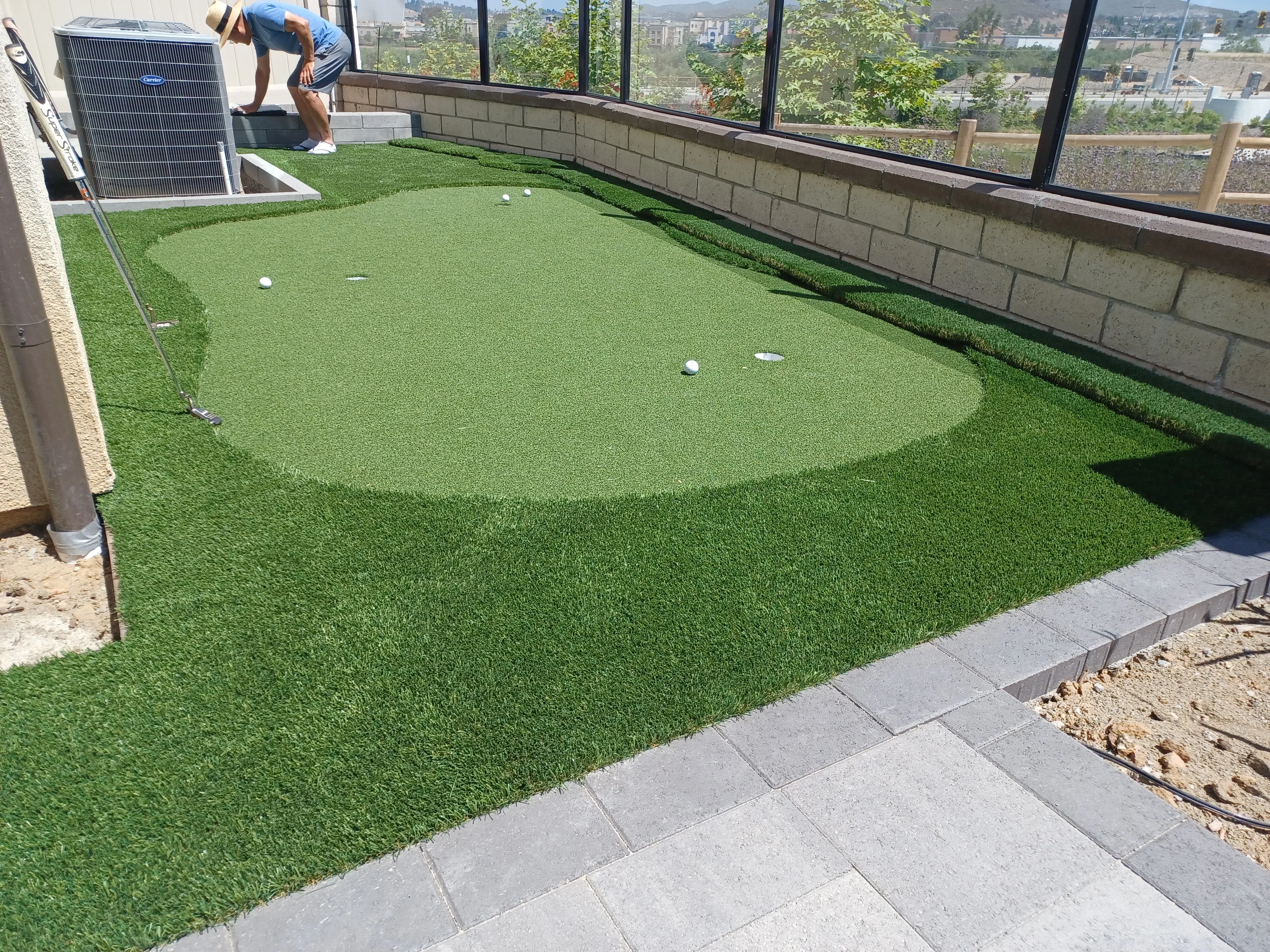 Synthetic turf putting green with concrete pavers, cinder block wall, and solar panel on rooftop
