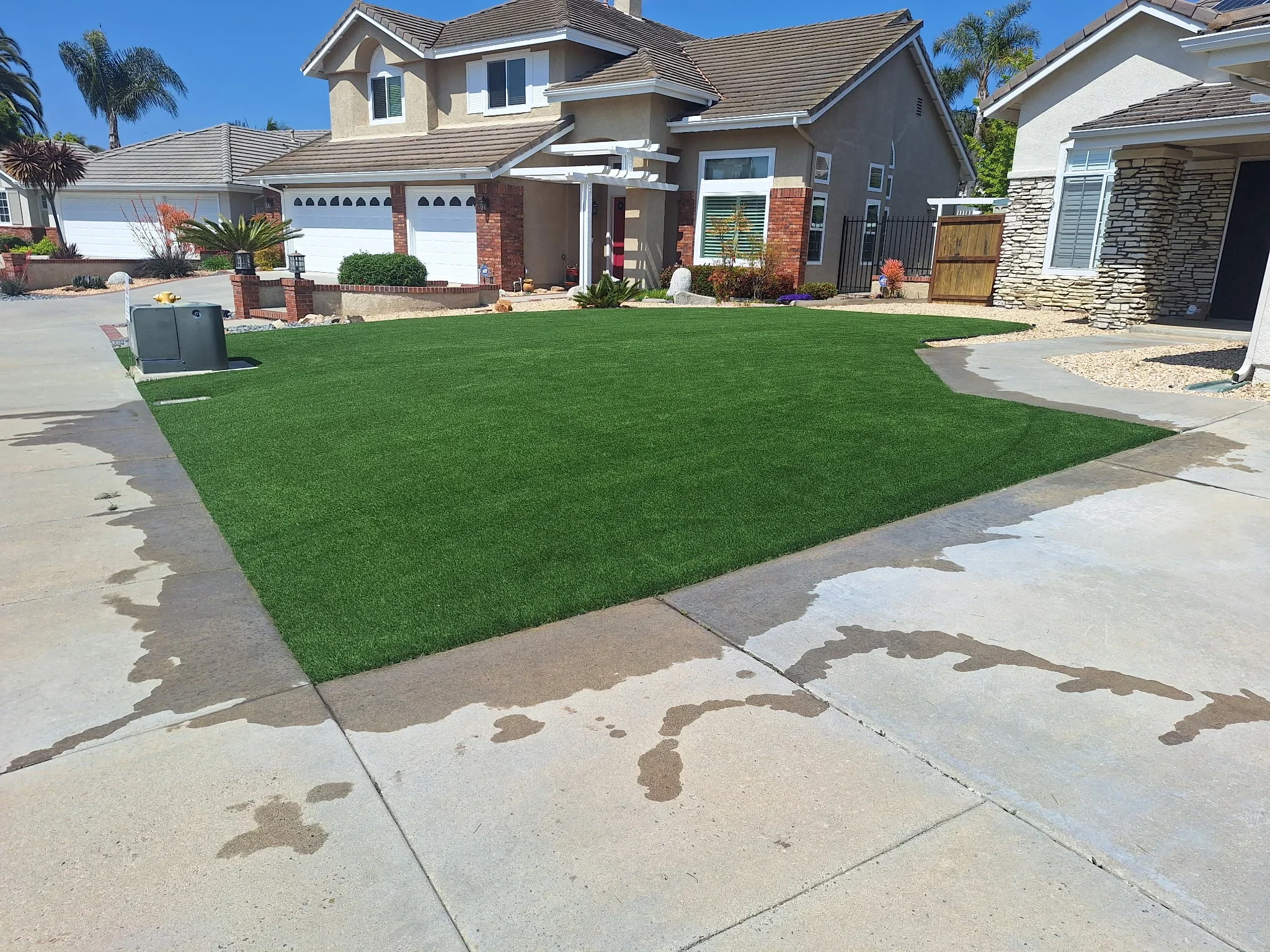 Synthetic turf lawn with concrete driveway and hardscape edging in front of residential home
