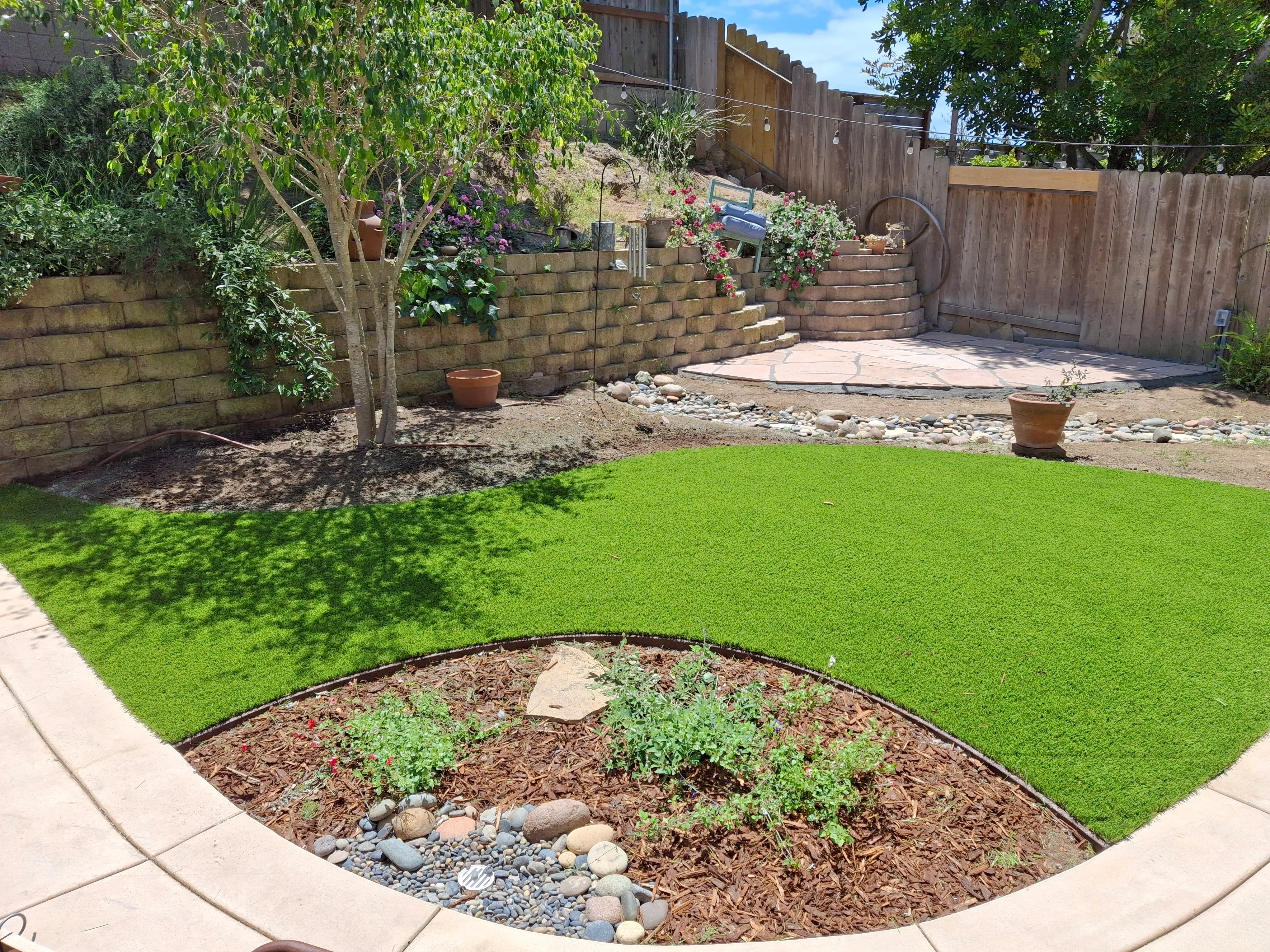 Concrete patio with curved planting bed, new sod lawn, retaining walls, and landscape edging